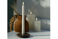 UYUNI Lighting（ウユニ・ライティング）は、デンマークのLEDで本物のキャンドル体験を再現するライティングブランドです。最大の魅力は、特許取得のユニークな「3Dフレーム（炎）」と、目で追ってしまうほど自然なフリッカー表現。灯りの芯が立ち上がるように見える立体的な炎は、見る角度によって表情が変わり、テーブル上のガラス器や壁面に繊細な陰影を落とします。見た目はクラシック、手触りはラグジュアリー、内部機構はイノベーティブ、伝統的なキャンドルの佇まいを、現代のテクノロジーで静かにアップデートしました。外装には本物のワックス（パラフィン加工の表面仕上げ）を用い、日中に置いてあるだけでも上質なオブジェのような存在感。夜は色温度のやさしい光で、北欧らしいhygge（ヒュッゲ）の空気を手軽にまとえます。インテリアの審美眼に応えるプロップとして完成度の高いLEDキャンドルです。