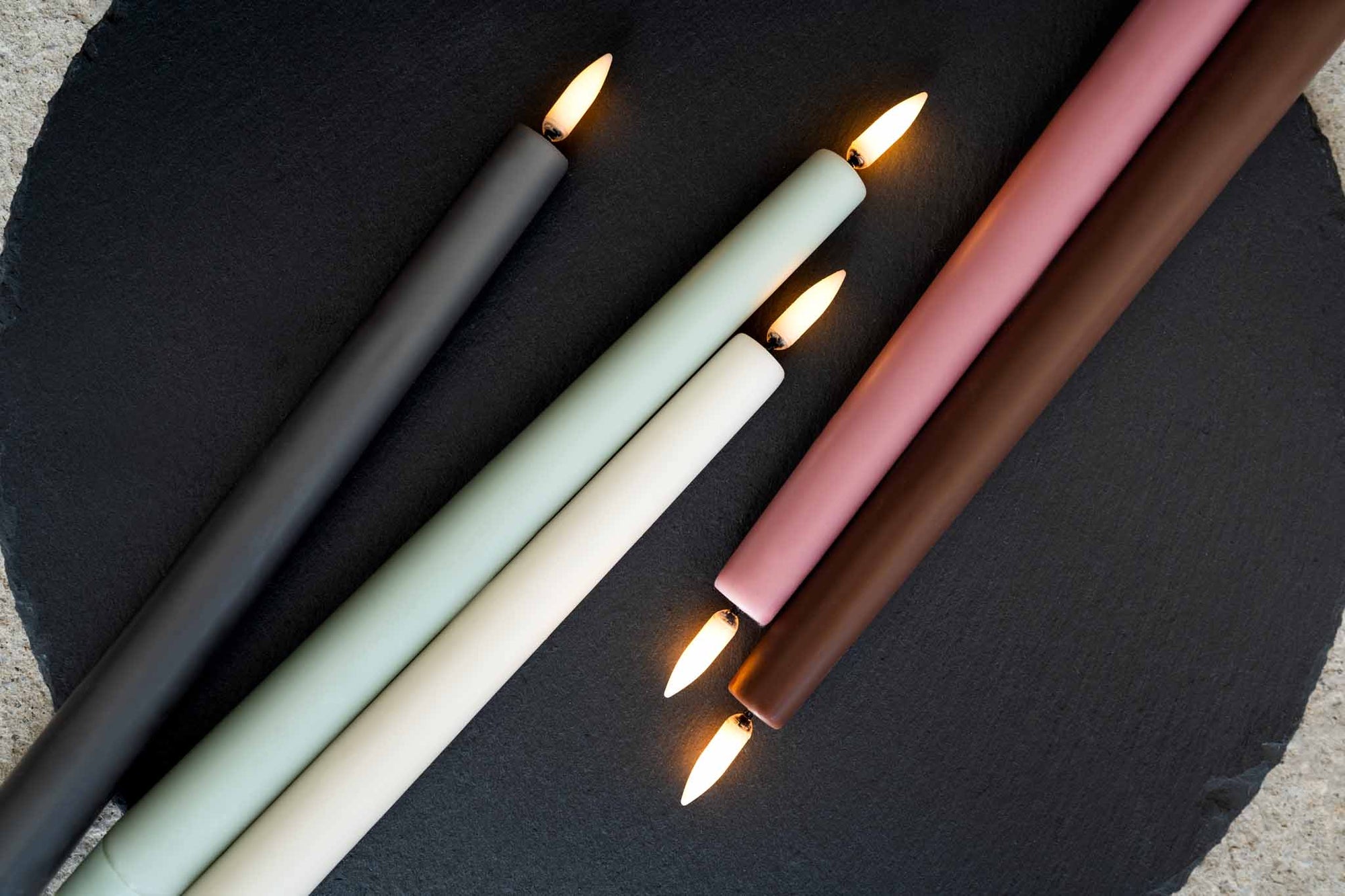 UYUNI Lighting（ウユニ・ライティング）は、デンマークのLEDで本物のキャンドル体験を再現するライティングブランドです。最大の魅力は、特許取得のユニークな「3Dフレーム（炎）」と、目で追ってしまうほど自然なフリッカー表現。灯りの芯が立ち上がるように見える立体的な炎は、見る角度によって表情が変わり、テーブル上のガラス器や壁面に繊細な陰影を落とします。見た目はクラシック、手触りはラグジュアリー、内部機構はイノベーティブ、伝統的なキャンドルの佇まいを、現代のテクノロジーで静かにアップデートしました。外装には本物のワックス（パラフィン加工の表面仕上げ）を用い、日中に置いてあるだけでも上質なオブジェのような存在感。夜は色温度のやさしい光で、北欧らしいhygge（ヒュッゲ）の空気を手軽にまとえます。インテリアの審美眼に応えるプロップとして完成度の高いLEDキャンドルです。