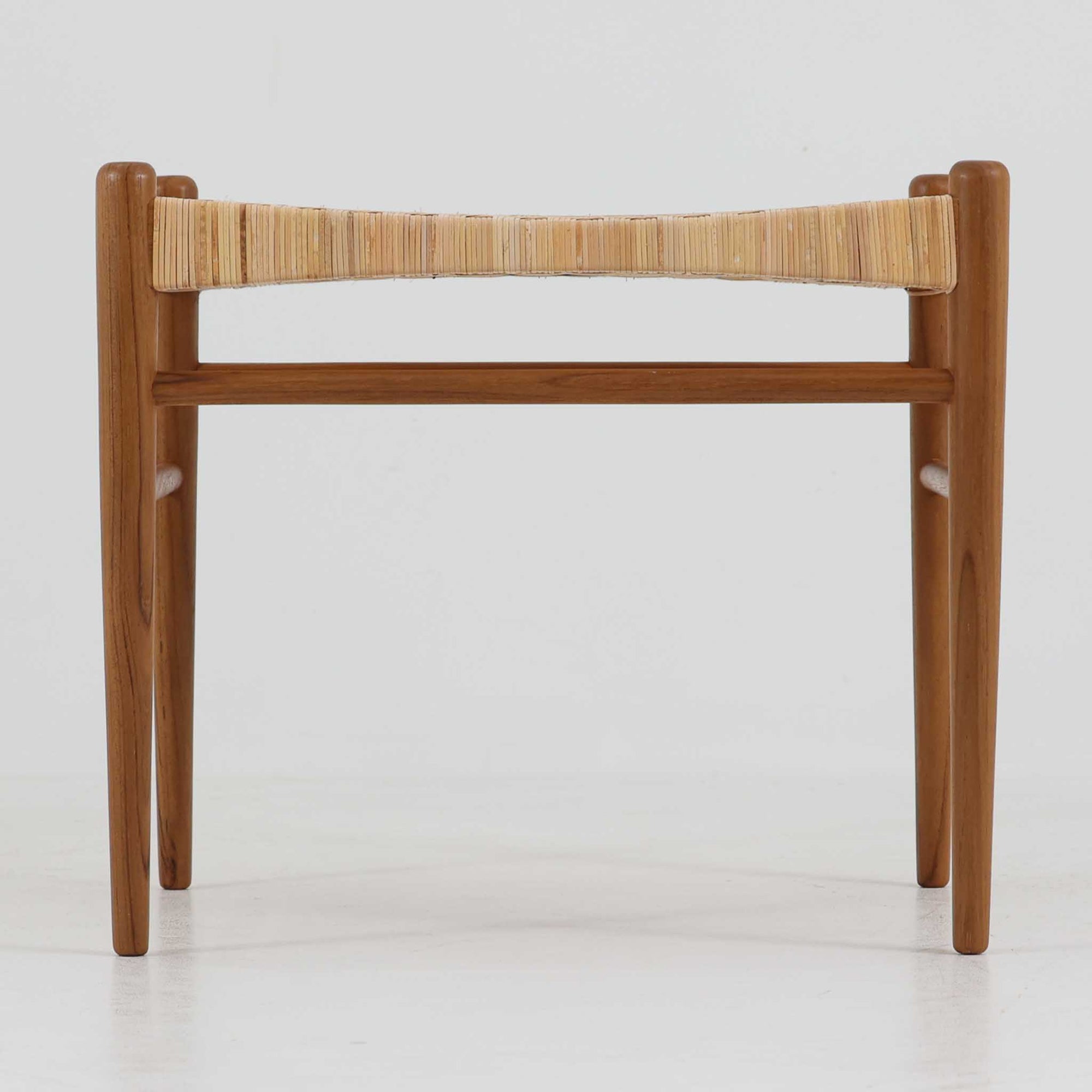 北欧デザインのスツールです。上質なチーク材フレームを丁寧に削り、シャープでスタイリッシュですが、柔らかい表情も持ち合わせたデザインに仕上げています。また、軽量ですが、しっかりとした造りになっています。座面の籐（ラタン）は上質で天然なもので細かい網目状に時間をかけて編み込まれています。使い込むほどにあめ色に変化し馴染んでくるのも天然素材の大きな魅力です。お部屋の片隅にクッションなどを添えて置いておくだけでもおしゃれです。必要なときにすっと出して使えます。複数スタッキングできるのも嬉しいです。