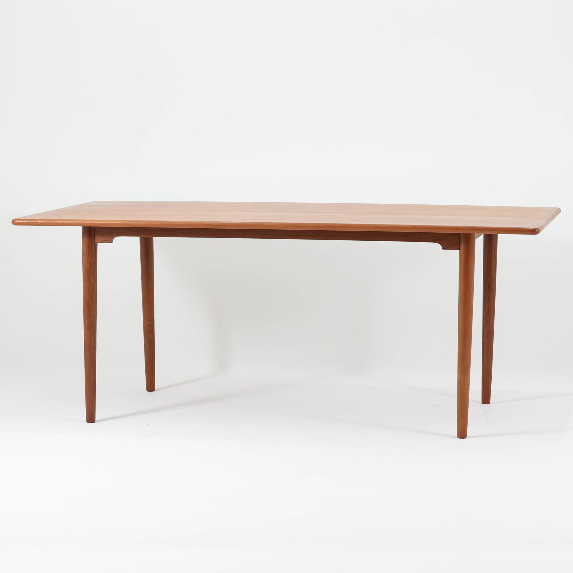 北欧モダンデザイン、180cm幅の大きな６人用ダイニングテーブルです。天板トップには見た目にも美しい上質なチーク突板を使用し、縁には贅沢に無垢材をジョイントしており、耐久力に加え曲線の美しさが際立っています。また、椅子を収納する際に干渉することが多い幕板ですが中央部を浅くすることで、干渉を軽減し、また見た目にも高級感を演出しています。通常安価な材質で仕上げられる幕板や天板裏面にも贅沢にチーク材天然木を使用しております。脚のポジションはやや内側にセットされスタイリッシュなデザインにも仕上がっています。
