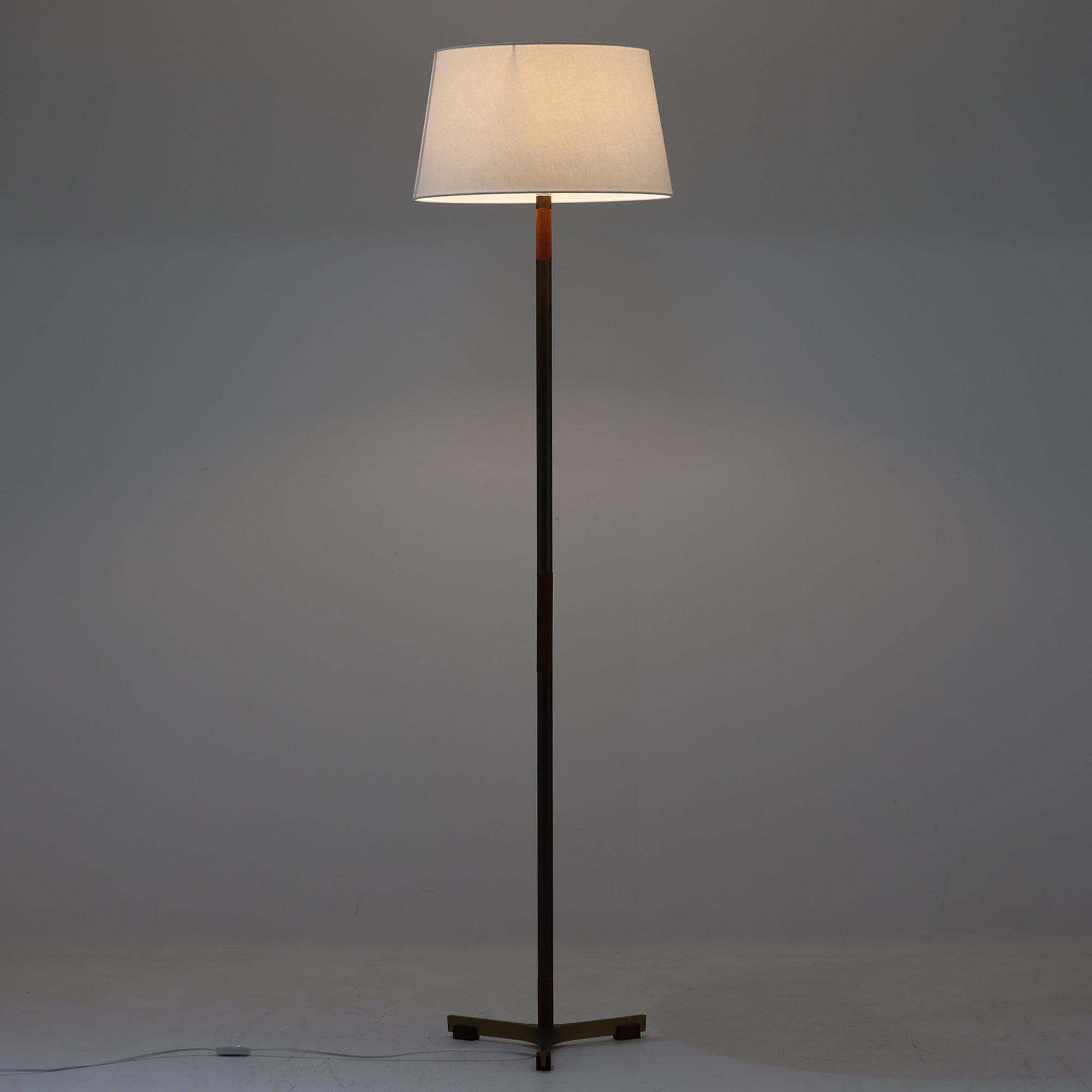Jo HammerborgがFog & Morupのために手がけた「Monolit」は、真鍮のシャフトにチーク材のアクセントを加えたミニマルで洗練されたフロアランプです。高さ164cmの堂々たるプロポーションに、Y字型の真鍮ベースが独自の存在感を放ち、リネンシェードを通した柔らかな光が空間に落ち着きを与えます。素材のコントラストと構造美が際立つ一台は、北欧ビンテージ照明の中でも特に希少な逸品といえるでしょう。