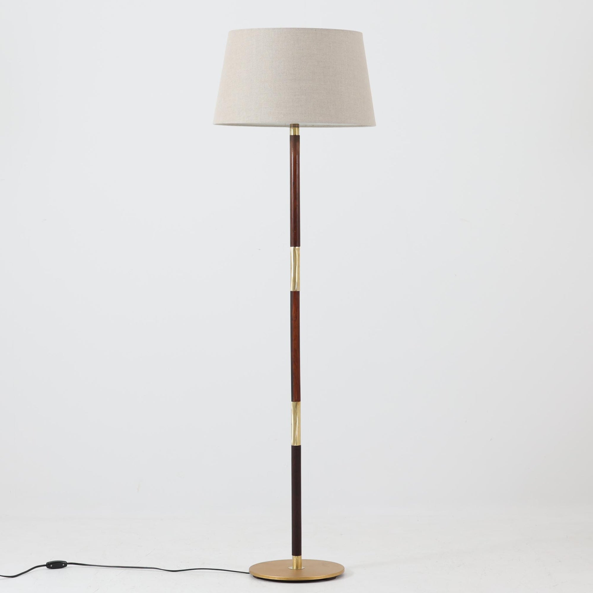 ローズウッド材の落ち着いた木肌と真鍮の輝きが美しく調和したデンマーク製のフロアランプは、直線的な支柱構造により空間をすっきりと演出し、天然リネンのシェードから柔らかな光が広がる上質な佇まいが魅力の北欧ビンテージ家具です。