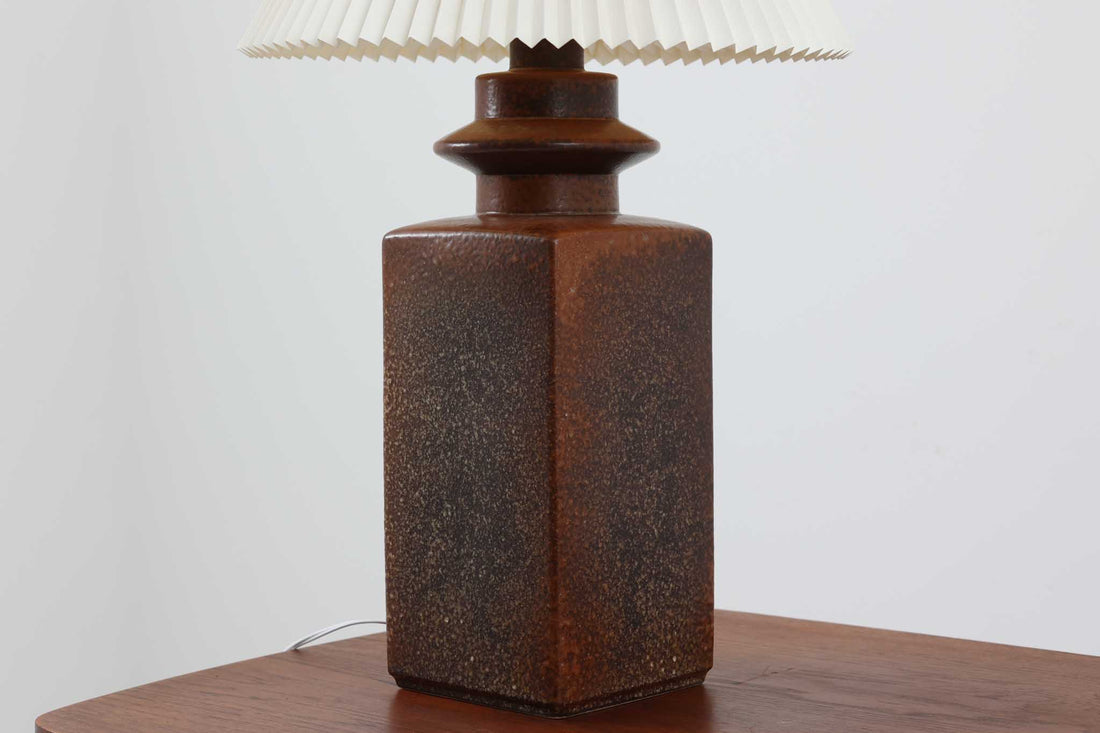 美しい質感の陶器ベースは、デンマークの名窯SOHOLm窯によるものです。SOHOLm窯は1835年から1996年まで営業しており、その高い技術と芸術性で知られる窯元でした。現在は廃業しているため、その作品はビンテージ品でのみ入手可能となっています。こちらの陶器ベースは深みのあるこげ茶色で、上品で落ち着いた雰囲気を醸し出しています。また、付属のシェードはLE KLINT社製で、職人の手仕事による特徴的な手折り加工が施されています。このシェードから零れるやわらかな光が、陶器ベースの質感と相まってお部屋全体を穏やかで心地よい空間に演出します。高さ74cmと大きめのサイズ感で、フロアランプとしてもお使いいただけます。リビングルームの隅に置くだけでなく、ベッドサイドや読書スペース、玄関ホールなど、さまざまなシーンで活躍します。