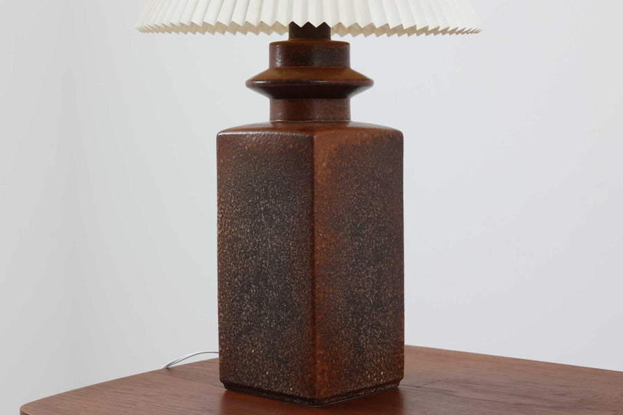 美しい質感の陶器ベースは、デンマークの名窯SOHOLm窯によるものです。SOHOLm窯は1835年から1996年まで営業しており、その高い技術と芸術性で知られる窯元でした。現在は廃業しているため、その作品はビンテージ品でのみ入手可能となっています。こちらの陶器ベースは深みのあるこげ茶色で、上品で落ち着いた雰囲気を醸し出しています。また、付属のシェードはLE KLINT社製で、職人の手仕事による特徴的な手折り加工が施されています。このシェードから零れるやわらかな光が、陶器ベースの質感と相まってお部屋全体を穏やかで心地よい空間に演出します。高さ74cmと大きめのサイズ感で、フロアランプとしてもお使いいただけます。リビングルームの隅に置くだけでなく、ベッドサイドや読書スペース、玄関ホールなど、さまざまなシーンで活躍します。