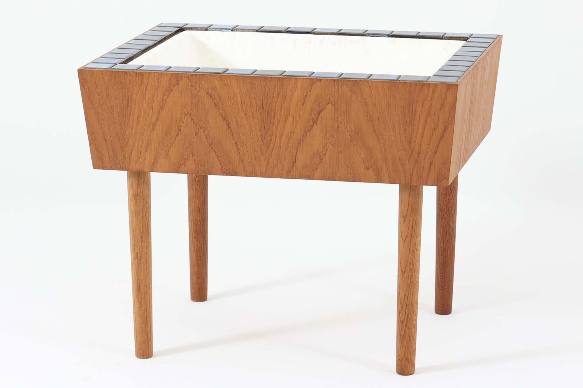 デンマーク製のプランターです。本体には良質なチーク材が使用されており、温かみのある木目が特徴です。さらに、縁部分には落ち着きのあるブルー色のタイルが装飾されており、シンプルでありながらもエレガントな雰囲気を醸し出しています。チーク材とタイルの組み合わせが絶妙で、どんなインテリアにも調和し、上品なアクセントとなる一品です。