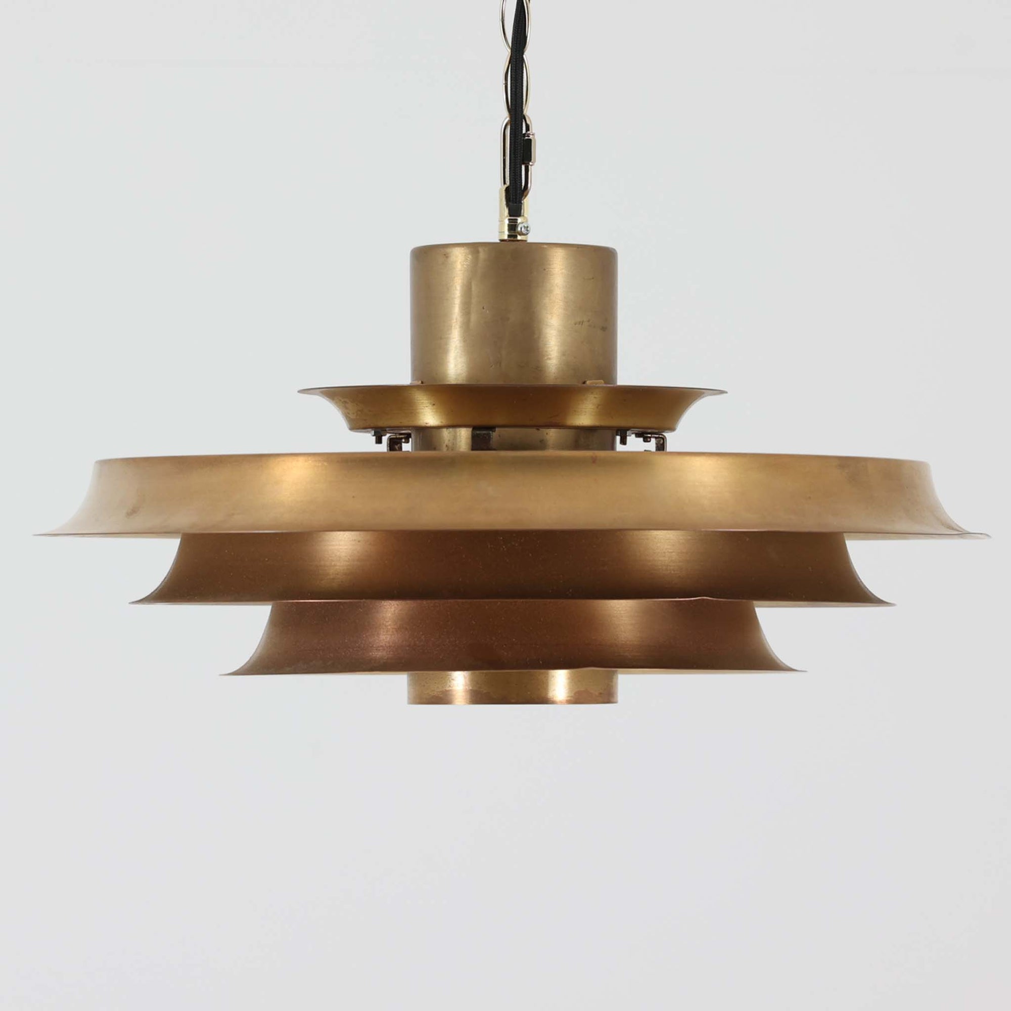 波打つように重なったシェードが印象的なデンマーク製のペンダントライト。無垢の真鍮によるしっかりとした重量感と、内側から放たれる柔らかな光が調和し、空間に温かみと品格を添えます。経年によって色味変化した真鍮は、この照明の歴史と個性を物語り、北欧ビンテージらしい味わい深い魅力を一層引き立てます。ダイニングやリビングのアクセントとして最適な一灯です。