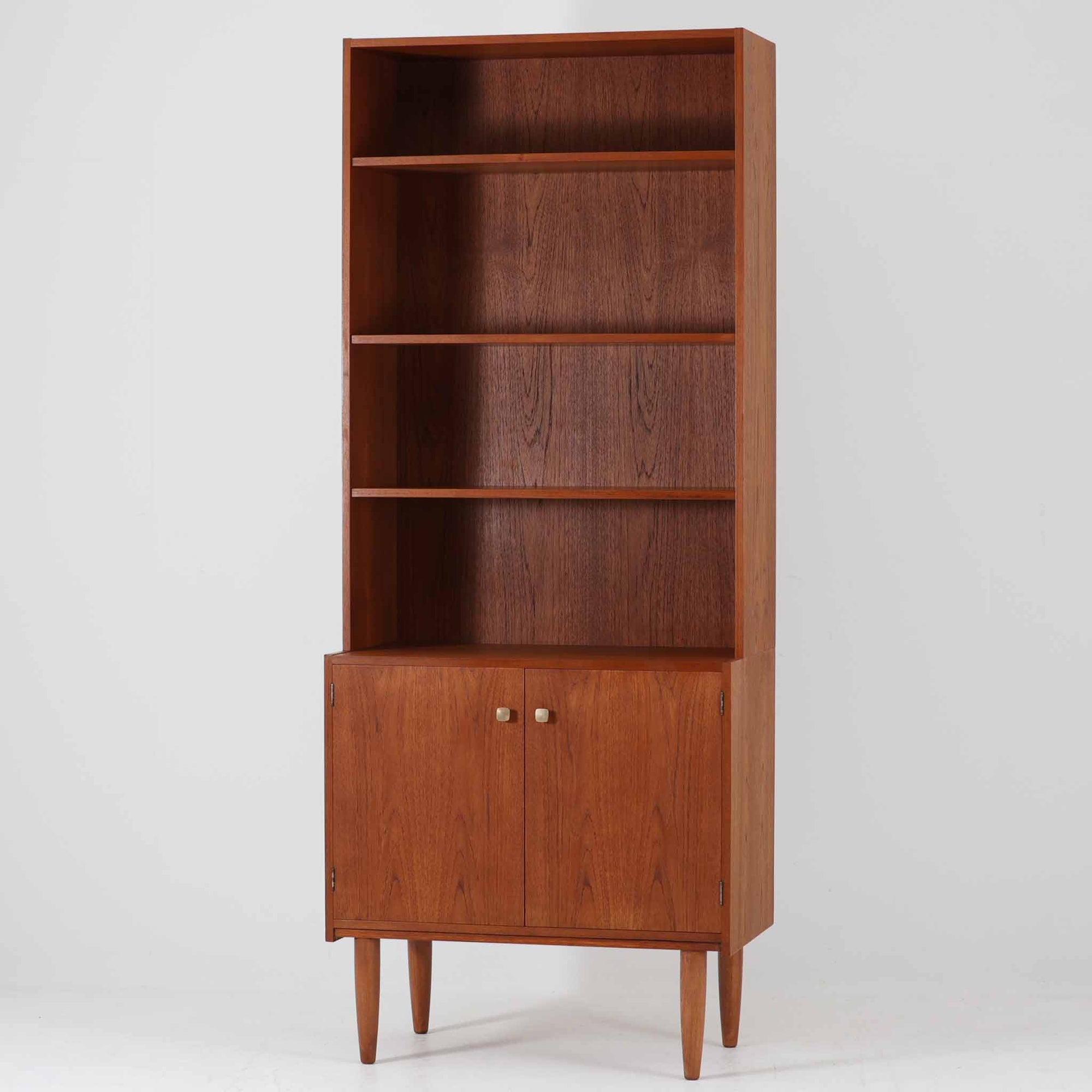デンマークのHorsens Mobelfabrik社によるディスプレイシェルフは、温かみあるチーク材を使用した端正な佇まいが魅力の一台です。上段には可動棚が4枚備わっており、書籍やオブジェなどのディスプレイに最適です。下段は観音開きの収納扉付きで、見せる収納と隠す収納を両立。すっきりとした脚部構造と洗練された金属取手がアクセントとなり、北欧らしい実用性と美しさを兼ね備えたビンテージ家具です。