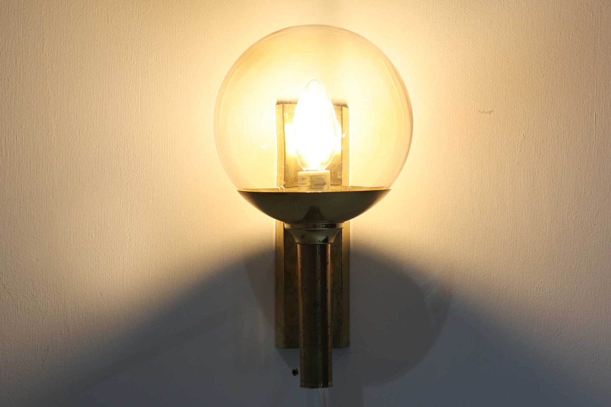 こちらは、Sven mejlstromによってデザインされた1960年代のウォールランプです。Sven mejlstromは、ノルウェーの照明デザイナーとして知られ、シンプルで機能的な美しさを追求したデザインを手掛けました。このランプは、真鍮とクリアガラスを組み合わせた美しいデザインが特徴で、ビンテージ品ならではの風合いが感じられます。大きなボール状のガラスシェードは光を柔らかく拡散し、空間に温かみと上品さを加えます。経年変化による真鍮部分の風合いも、時間を経た美しさを感じさせる魅力的な要素です。シンプルでありながらも印象的なこのウォールランプは、どんなインテリアにも調和し、エレガントなアクセントを与えてくれる一品です。