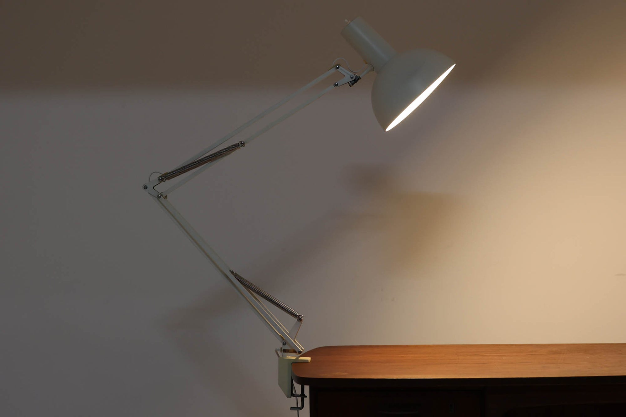 デンマークより買い付けたLouis Poulsen社製のデスクランプです。現行品では販売されていない希少なモデルで、シンプルながら機能的なデザインが特徴です。クランプタイプのため、置く場所を選ばず使用可能。最大板厚5cmまでの場所に取り付けることができるため、デスクやテーブルにしっかり固定してお使いいただけます。アーム部分は可動式で、光の角度を自由に調整できる設計になっており、デスクワークや読書、細かい作業にも最適です。ビンテージ品ならではの風合いが魅力的で、使い込まれたスチールの質感が独特の味わいを醸し出しています。