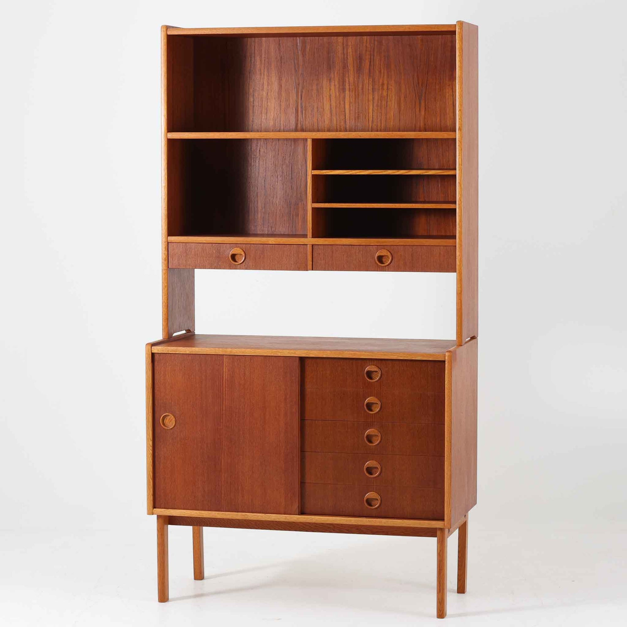 チーク材とオーク材を組み合わせたこちらのオープンシェルフは、スウェーデン製の北欧ビンテージ品で、幅85cmのコンパクトなサイズ感ながらも、引き出しや仕切り棚、スライド扉など多彩な収納機能を備えた実用的な一台です。温かみのある木の風合いと丸型の取手が、柔らかな印象を与えつつ、細部にまで配慮された職人技が感じられ、リビングや書斎の収納棚としてはもちろん、お気に入りの器や小物のディスプレイにも適しています。