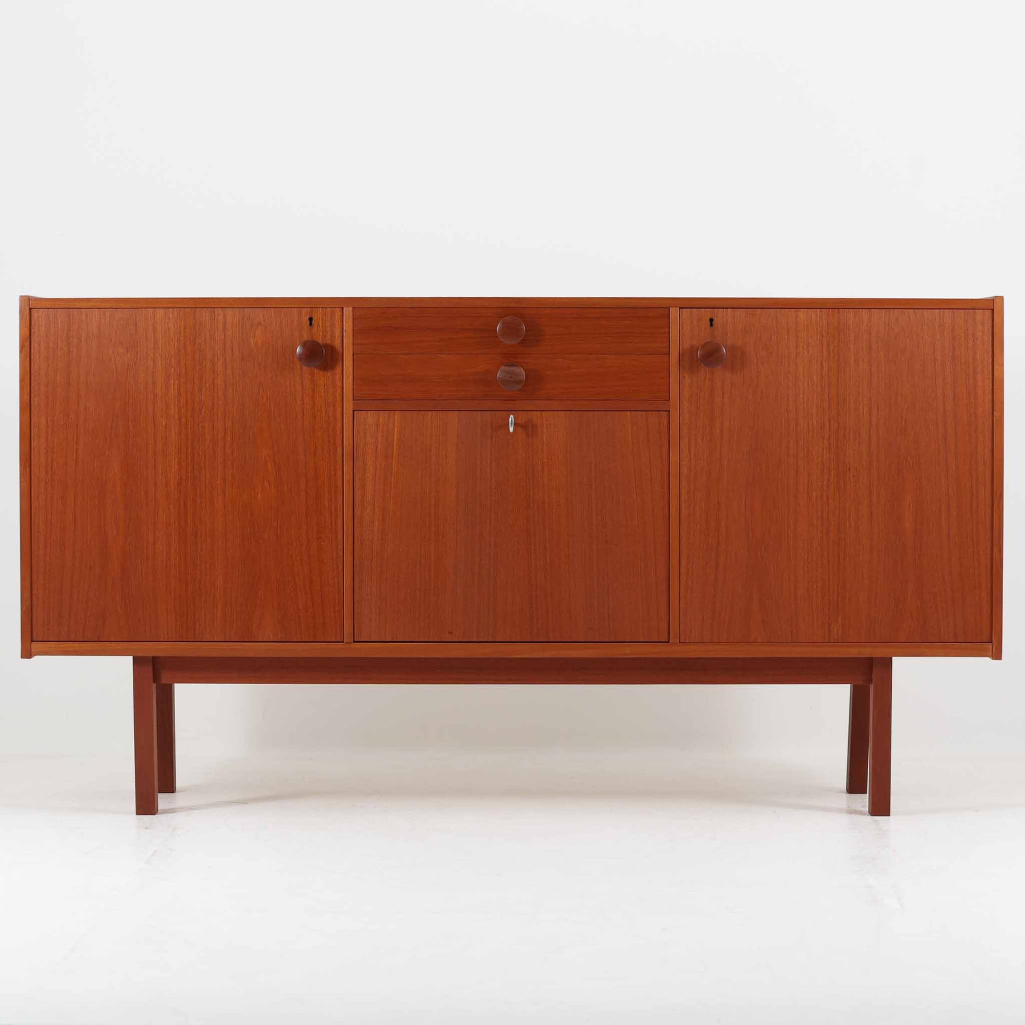 スウェーデンのBreox Moblerによるこちらのキッチンキャビネットは、温かみのあるチーク材を使用した北欧ビンテージ家具で、すっきりと直線的なフォルムと円形の木製取手が印象的な一台です。引き出し内には仕切り付きの収納も備え、カトラリーや小物の整理に便利です。扉内部は棚板付きで収納力にも優れ、中央の鍵付き扉はフラップ式でバースペースや食器収納としても活用できます。端正な佇まいと経年による木肌の深い色合いが空間に落ち着きを与える、実用性と存在感を兼ね備えた逸品です。