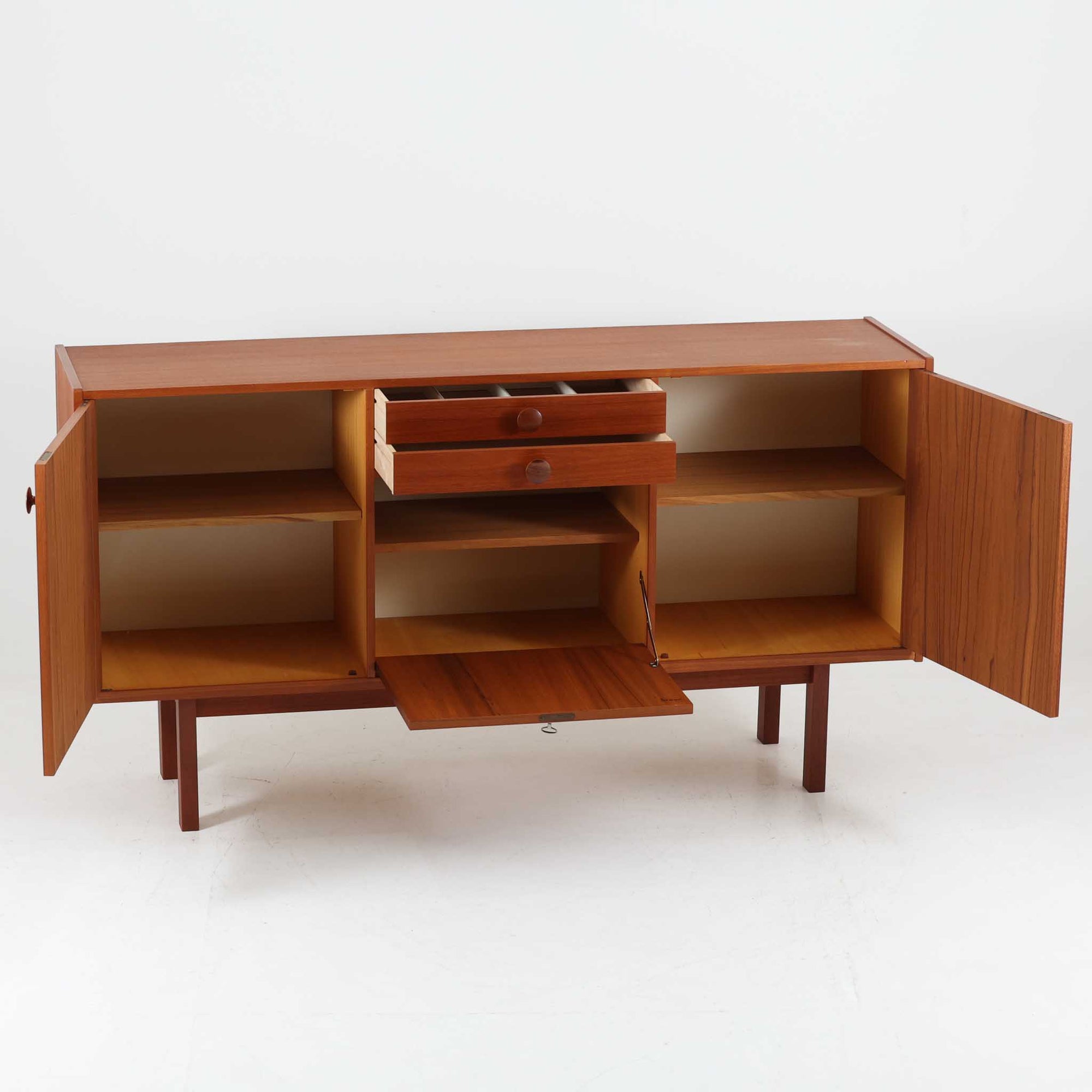 スウェーデンのBreox Moblerによるこちらのキッチンキャビネットは、温かみのあるチーク材を使用した北欧ビンテージ家具で、すっきりと直線的なフォルムと円形の木製取手が印象的な一台です。引き出し内には仕切り付きの収納も備え、カトラリーや小物の整理に便利です。扉内部は棚板付きで収納力にも優れ、中央の鍵付き扉はフラップ式でバースペースや食器収納としても活用できます。端正な佇まいと経年による木肌の深い色合いが空間に落ち着きを与える、実用性と存在感を兼ね備えた逸品です。