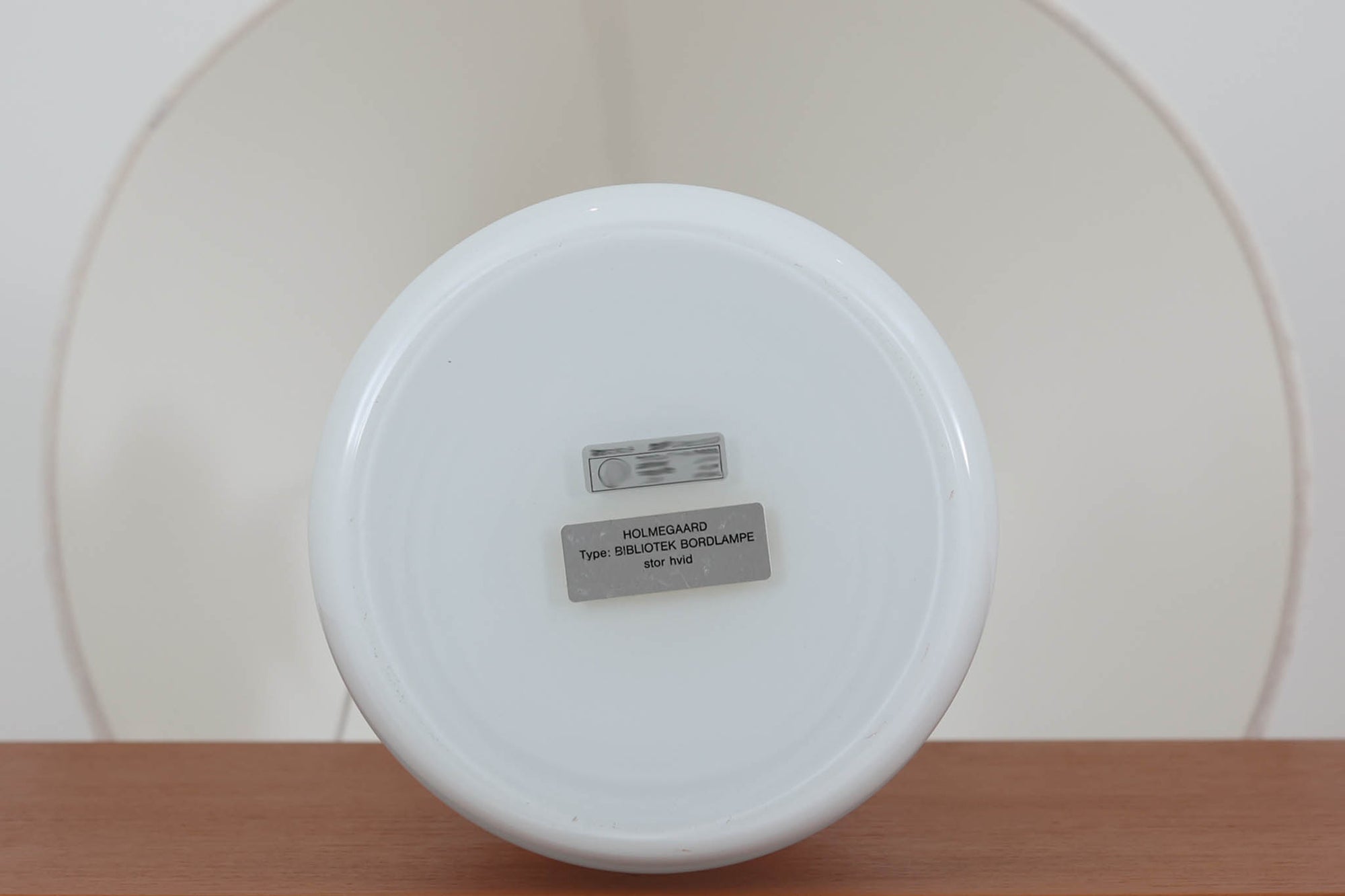 著名なデザイナー、Sidse Werner（シセ・ヴェルナー）による「BIBLIOTEK」のテーブルランプです。ペンダントランプはよく見かけますが、テーブルランプは非常に珍しいモデルです。ホルムガードならではの厚みのある高品質なガラスを使用しており、点灯するとシェードを通して柔らかな温かみのある光が広がり、空間を優雅に照らします。高さ64cmの大型サイズで存在感があり、リビングや書斎、ベッドサイドなど、あらゆるインテリアに美しく調和します。