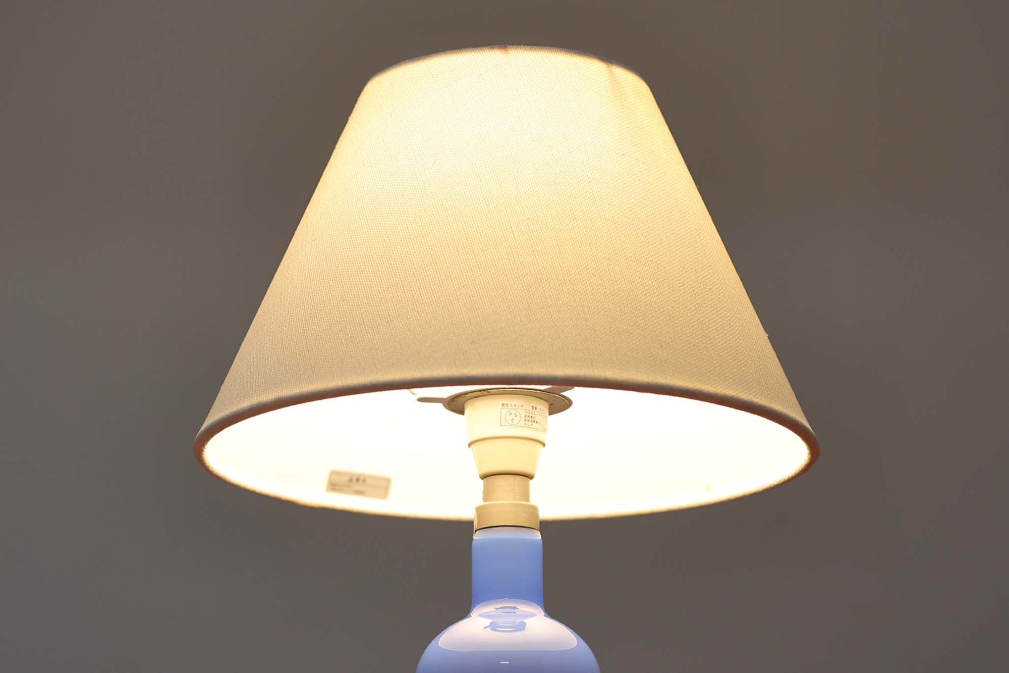 こちらはRoyal Copenhagen社製のテーブルランプで、元々はホルムガード社で製造されていたものです。1985年にRoyal Copenhagen社に買収されたため、比較的最近製造された個体と考えられます。淡い青のガラスベースは滑らかなラインが特徴で、真鍮との組み合わせが美しい一品です。デンマーク製のファブリックシェードが付属しています。