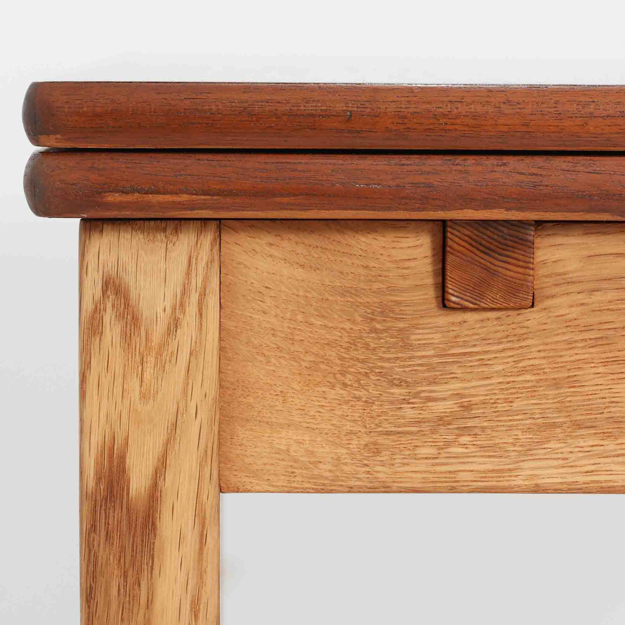 Ejner Larsen &amp; Aksel Bender Madsenが手掛け、Naestved Mobelfabrikで製作されたエクステンションダイニングテーブルは、チーク材の天板とオーク材の脚部を組み合わせた北欧ビンテージらしい上質な佇まいが魅力です。直線的で端正なフォルムの中に、天板縁の丁寧な面取りや幕板の滑らかな造形など、当時の高い職人技が随所に感じられます。幅120cmから最大230cmまで伸長可能な構造により、日常使いから来客時まで柔軟に対応でき、空間や人数に合わせた使い方が可能です。経年変化によって深みを増した木肌の表情が、長く愛用されてきたビンテージならではの存在感を放ち、ダイニングの主役として落ち着きと品格を添えてくれる一台です。脚先には床へのダメージや汚れを防ぐためにチーク材がジョイントされており、実用性を考慮した当時の設計思想がうかがえます。また、裏面には「SKM」の刻印が確認でき、スウェーデン軍（Svenska KrigsMakten）の備品として使用されていたことを示す、背景のある希少な個体です。