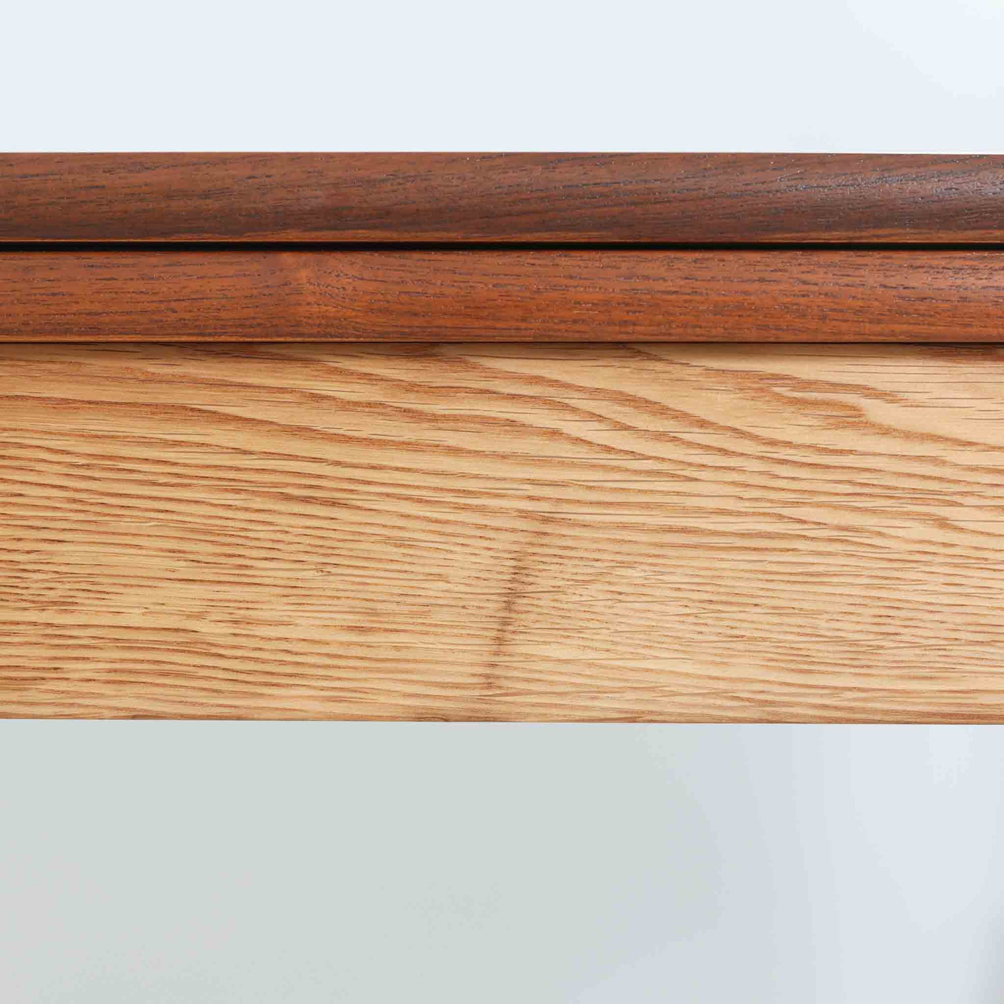 Ejner Larsen &amp; Aksel Bender Madsenが手掛け、Naestved Mobelfabrikで製作されたエクステンションダイニングテーブルは、チーク材の天板とオーク材の脚部を組み合わせた北欧ビンテージらしい上質な佇まいが魅力です。直線的で端正なフォルムの中に、天板縁の丁寧な面取りや幕板の滑らかな造形など、当時の高い職人技が随所に感じられます。幅120cmから最大230cmまで伸長可能な構造により、日常使いから来客時まで柔軟に対応でき、空間や人数に合わせた使い方が可能です。経年変化によって深みを増した木肌の表情が、長く愛用されてきたビンテージならではの存在感を放ち、ダイニングの主役として落ち着きと品格を添えてくれる一台です。脚先には床へのダメージや汚れを防ぐためにチーク材がジョイントされており、実用性を考慮した当時の設計思想がうかがえます。また、裏面には「SKM」の刻印が確認でき、スウェーデン軍（Svenska KrigsMakten）の備品として使用されていたことを示す、背景のある希少な個体です。