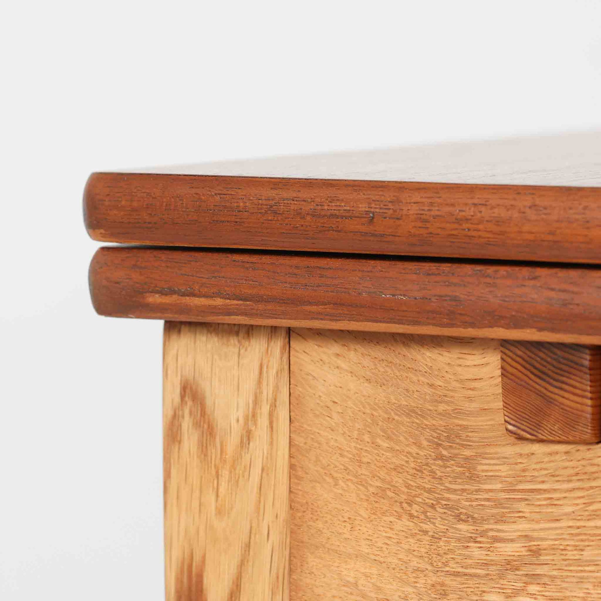 Ejner Larsen &amp; Aksel Bender Madsenが手掛け、Naestved Mobelfabrikで製作されたエクステンションダイニングテーブルは、チーク材の天板とオーク材の脚部を組み合わせた北欧ビンテージらしい上質な佇まいが魅力です。直線的で端正なフォルムの中に、天板縁の丁寧な面取りや幕板の滑らかな造形など、当時の高い職人技が随所に感じられます。幅120cmから最大230cmまで伸長可能な構造により、日常使いから来客時まで柔軟に対応でき、空間や人数に合わせた使い方が可能です。経年変化によって深みを増した木肌の表情が、長く愛用されてきたビンテージならではの存在感を放ち、ダイニングの主役として落ち着きと品格を添えてくれる一台です。脚先には床へのダメージや汚れを防ぐためにチーク材がジョイントされており、実用性を考慮した当時の設計思想がうかがえます。また、裏面には「SKM」の刻印が確認でき、スウェーデン軍（Svenska KrigsMakten）の備品として使用されていたことを示す、背景のある希少な個体です。