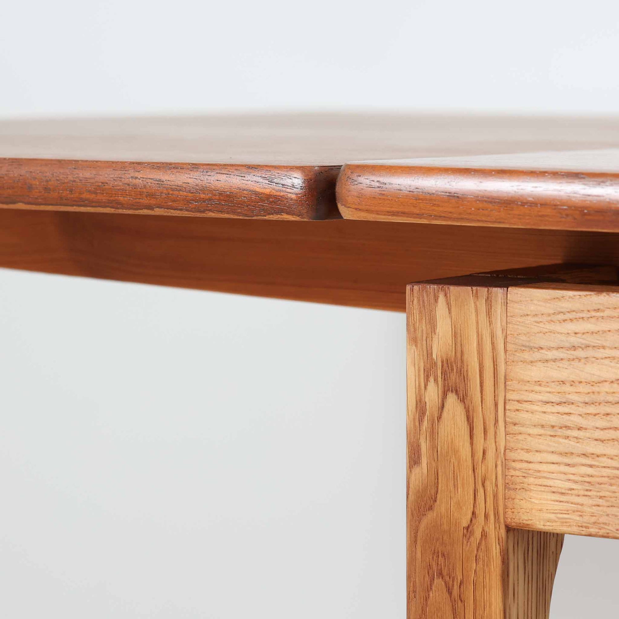 Ejner Larsen &amp; Aksel Bender Madsenが手掛け、Naestved Mobelfabrikで製作されたエクステンションダイニングテーブルは、チーク材の天板とオーク材の脚部を組み合わせた北欧ビンテージらしい上質な佇まいが魅力です。直線的で端正なフォルムの中に、天板縁の丁寧な面取りや幕板の滑らかな造形など、当時の高い職人技が随所に感じられます。幅120cmから最大230cmまで伸長可能な構造により、日常使いから来客時まで柔軟に対応でき、空間や人数に合わせた使い方が可能です。経年変化によって深みを増した木肌の表情が、長く愛用されてきたビンテージならではの存在感を放ち、ダイニングの主役として落ち着きと品格を添えてくれる一台です。脚先には床へのダメージや汚れを防ぐためにチーク材がジョイントされており、実用性を考慮した当時の設計思想がうかがえます。また、裏面には「SKM」の刻印が確認でき、スウェーデン軍（Svenska KrigsMakten）の備品として使用されていたことを示す、背景のある希少な個体です。