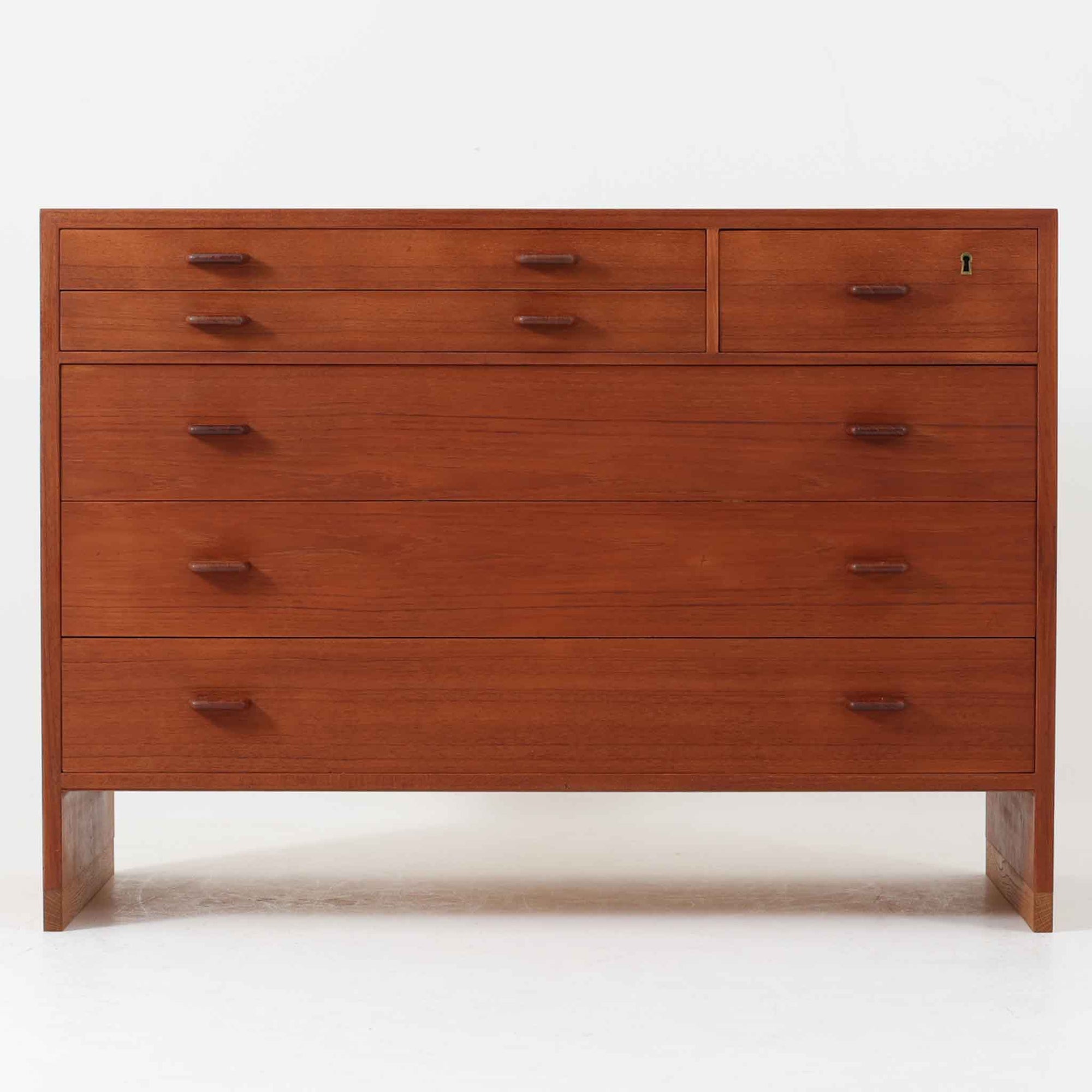 Hans J. Wegnerが手掛けたこちらの多段チェストは、Ry Mobler社によって1962年に製造されたもので、チーク材とオーク材の美しいコントラストが印象的な一台です。チーク材仕様のモデルは現存数が少なく、希少です。端正なフォルムと落ち着いた木肌は、寝室やリビングに上質な温もりをもたらします。引き出し内部にはフェルトが敷かれ、最上段には鍵付きの収納も備わっており、細部にまでこだわった設計が魅力です。※写真には写っておりませんが、鍵が1点付属いたします。実用性と美しさを兼ね備えた、北欧ビンテージらしい逸品です。