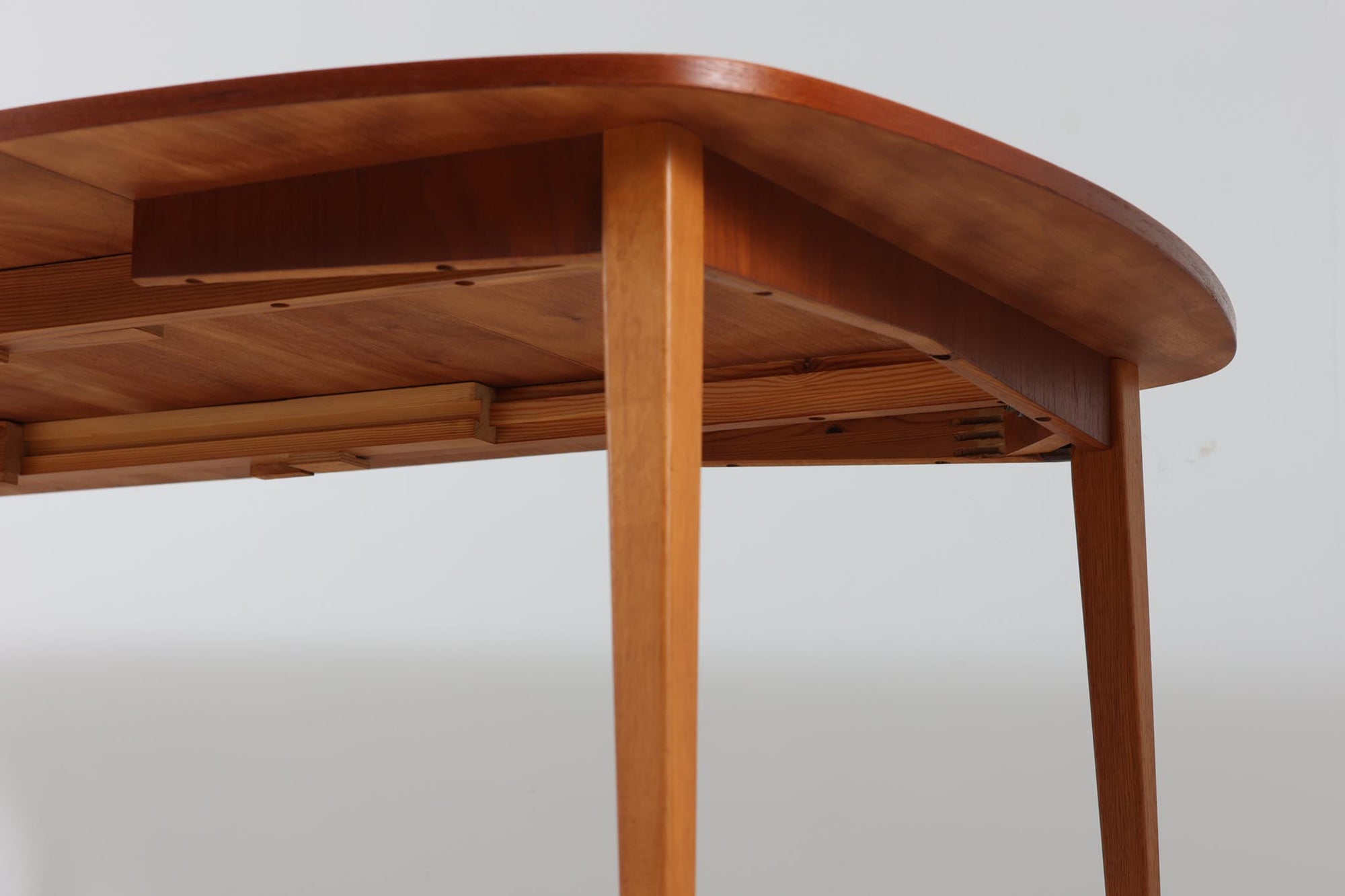 こちらはスウェーデンで買い付けたエクステンションダイニングテーブルです。天板は、珍しいラウンドスクエアの形状を採用しており、柔らかな印象と洗練されたデザインが魅力です。脚部は左右に開く構造で安定感があり、幕板は中央部分に向かってカットされているため、椅子の出し入れや座り心地にも配慮されています。また、来客時には付属の拡張板を使用することで、天板を簡単に広げられ、大人数での食事にも対応可能です。使い手の利便性を追求した設計が光る一品です。素材には、良質なチーク材とオーク材を使用しており、木目の美しさや温かみを感じられます。北欧家具ならではの高いデザイン性と実用性を兼ね備えたダイニングテーブルをぜひお楽しみください。