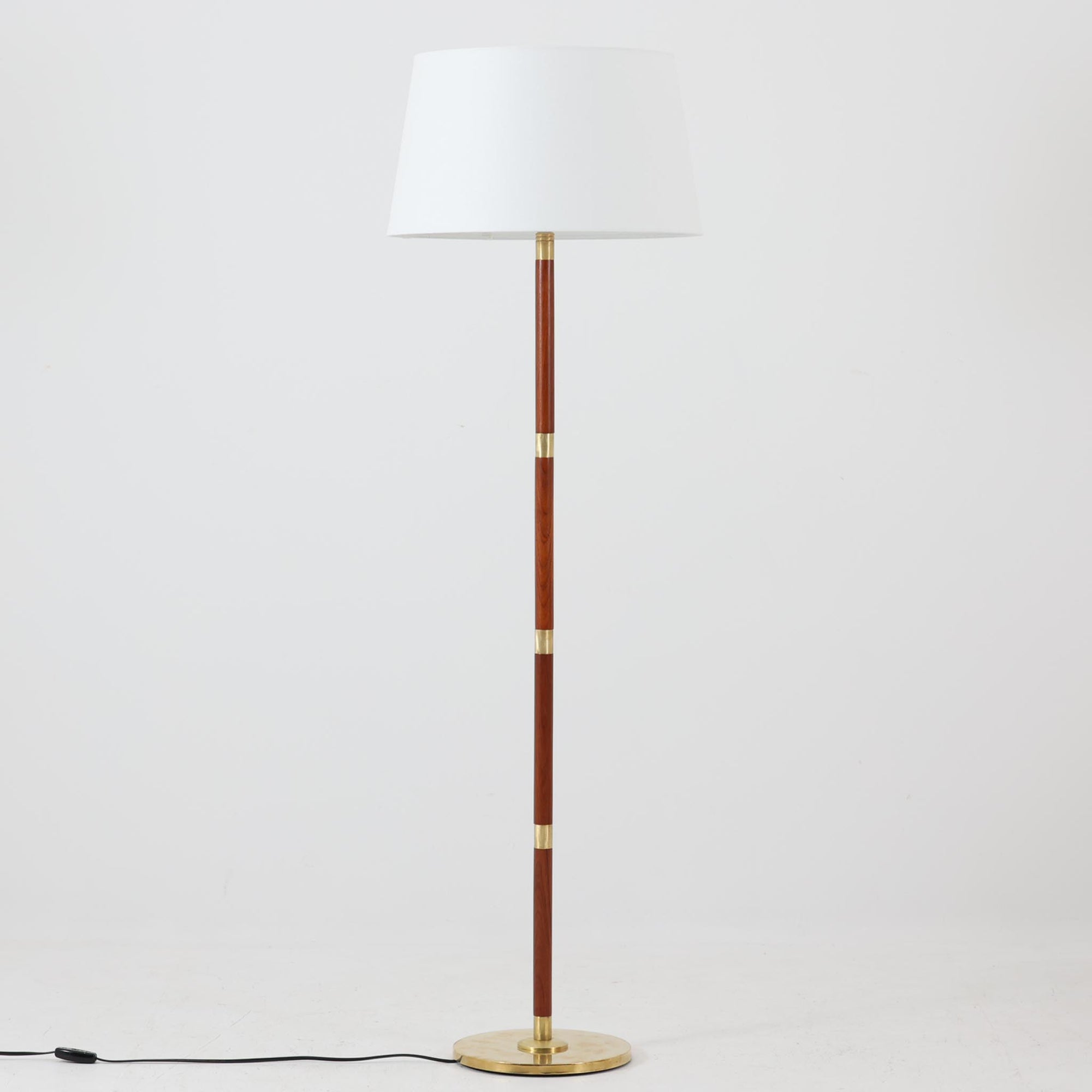 真鍮とチーク材のコンビネーションが美しいデンマーク製のフロアランプは、節目ごとに金属パーツを配した細身の支柱と、柔らかな光を拡げるリネンシェードが特徴で、消灯時も彫刻のような存在感を放つ一台です。高さ135cmと扱いやすく、ソファサイドやベッドサイドに取り入れることで、空間に品格と温もりを添えてくれます。