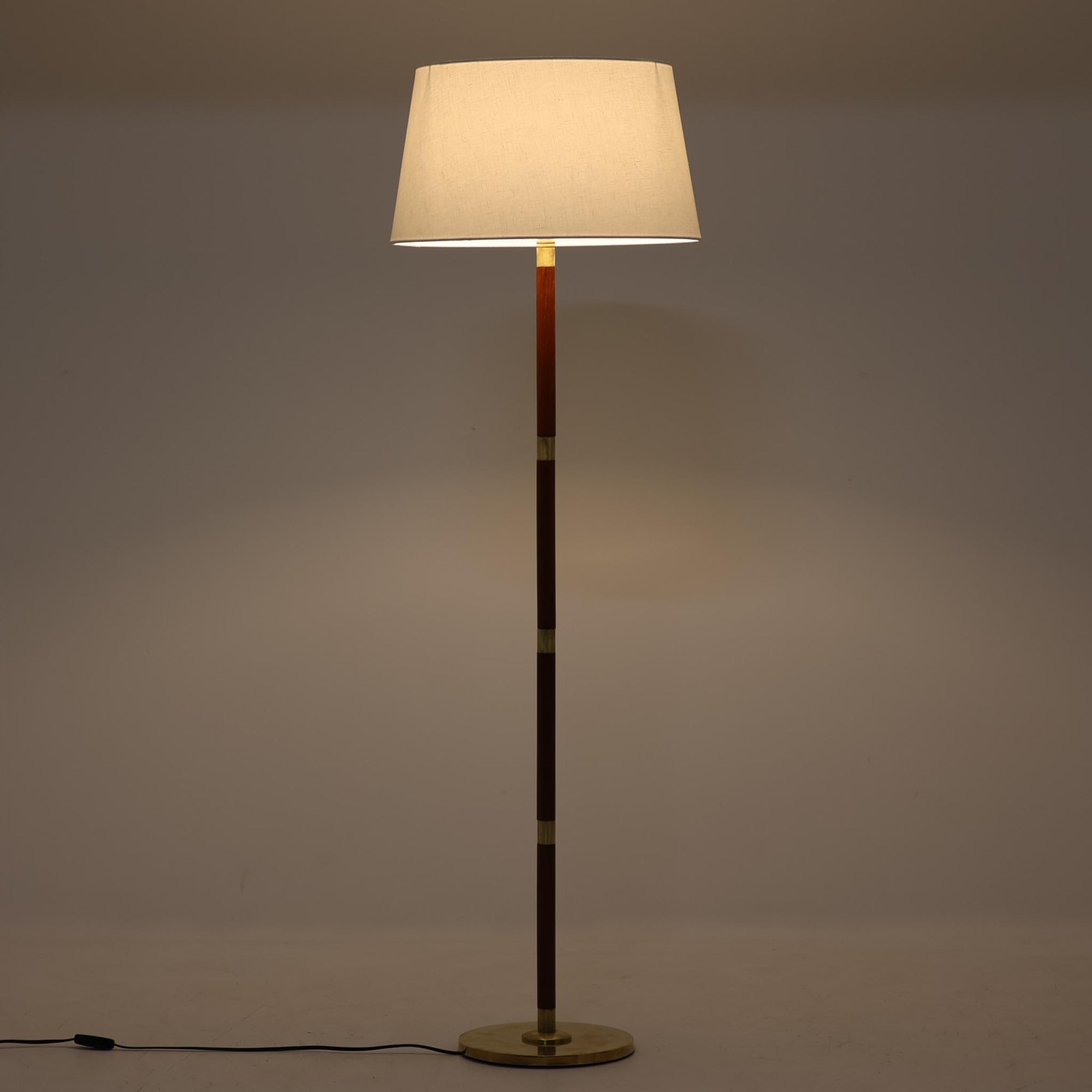真鍮とチーク材のコンビネーションが美しいデンマーク製のフロアランプは、節目ごとに金属パーツを配した細身の支柱と、柔らかな光を拡げるリネンシェードが特徴で、消灯時も彫刻のような存在感を放つ一台です。高さ135cmと扱いやすく、ソファサイドやベッドサイドに取り入れることで、空間に品格と温もりを添えてくれます。