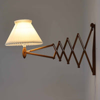 Erik Hansen（エリック・ハンセン）がデザインし、Le Klint（レ・クリント）から発表されたブラケットランプModel 332です。こちらは現行品には見られない一回り大きなサイズ感が特徴で、存在感のある佇まいを持っています。オーク材のナチュラルな風合いと、職人によるプリーツシェードが織りなす柔らかな光が空間を優しく包み込みます。アコーディオン式のアームは伸縮可能で、ベッドサイドやリビングの読書灯としても活躍する実用性の高い一品です。