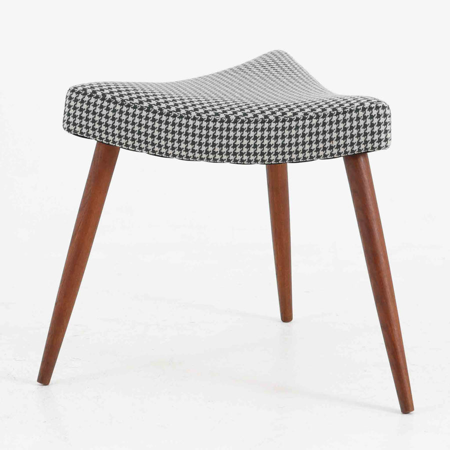 デンマーク製スツールです。3本脚の軽やかなフォルムに、チーク材の温もりが感じられる北欧ビンテージらしい佇まいが魅力です。三角形の座面は座り心地を考慮した絶妙な曲面で構成され、張地は千鳥格子柄のファブリックで仕上げました。玄関や寝室の補助椅子としてはもちろん、オットマンとしても活躍します。経年により深みを増したチーク材の脚が空間に上品な印象を与える一脚です。
