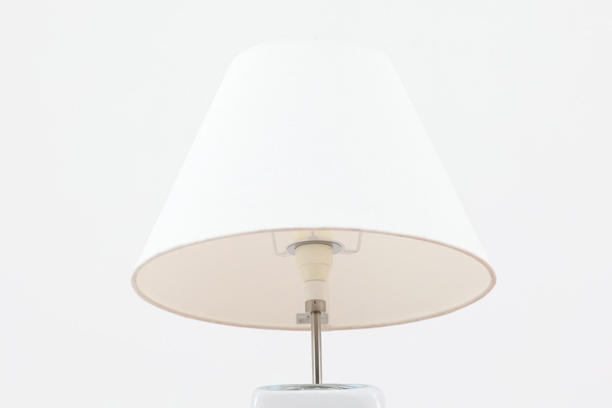 Per Lütken（ペル・ルッケン）が1980年代にデザインした「Kubus（キューブス）」シリーズのテーブルランプです。名前の通り、立方体（キューブ）をモチーフにしたホルムガードならではの厚みのある高品質なガラスが使用されており、点灯すると柔らかな光が広がり、空間に温かみと落ち着きを与えます。細いメタルの支柱が全体を引き締め、ミニマルで洗練されたデザインを際立たせています。大中小のサイズ展開がある中で、こちらは中サイズのモデルです。