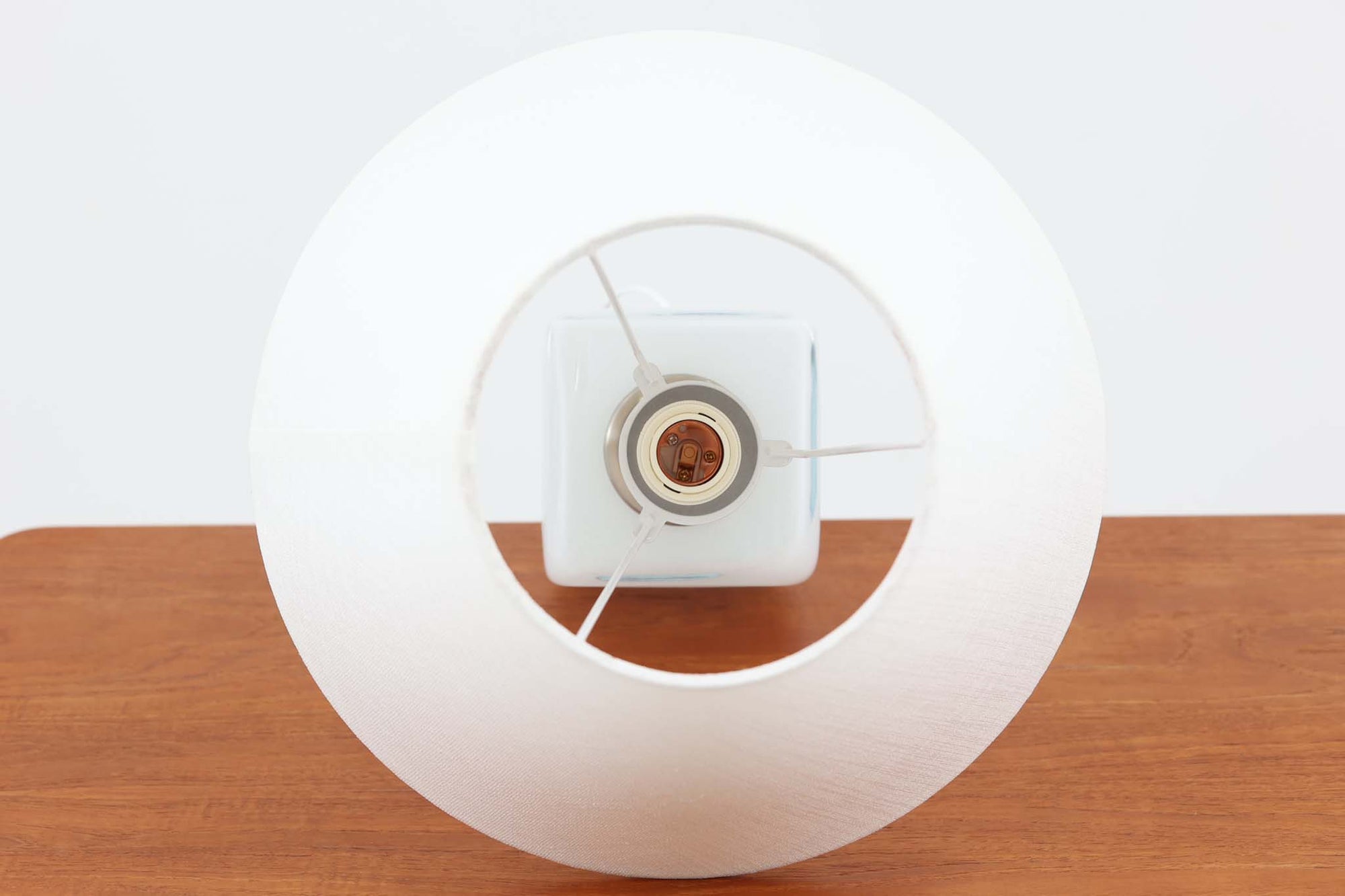 Per Lütken（ペル・ルッケン）が1980年代にデザインした「Kubus（キューブス）」シリーズのテーブルランプです。名前の通り、立方体（キューブ）をモチーフにしたホルムガードならではの厚みのある高品質なガラスが使用されており、点灯すると柔らかな光が広がり、空間に温かみと落ち着きを与えます。細いメタルの支柱が全体を引き締め、ミニマルで洗練されたデザインを際立たせています。大中小のサイズ展開がある中で、こちらは中サイズのモデルです。