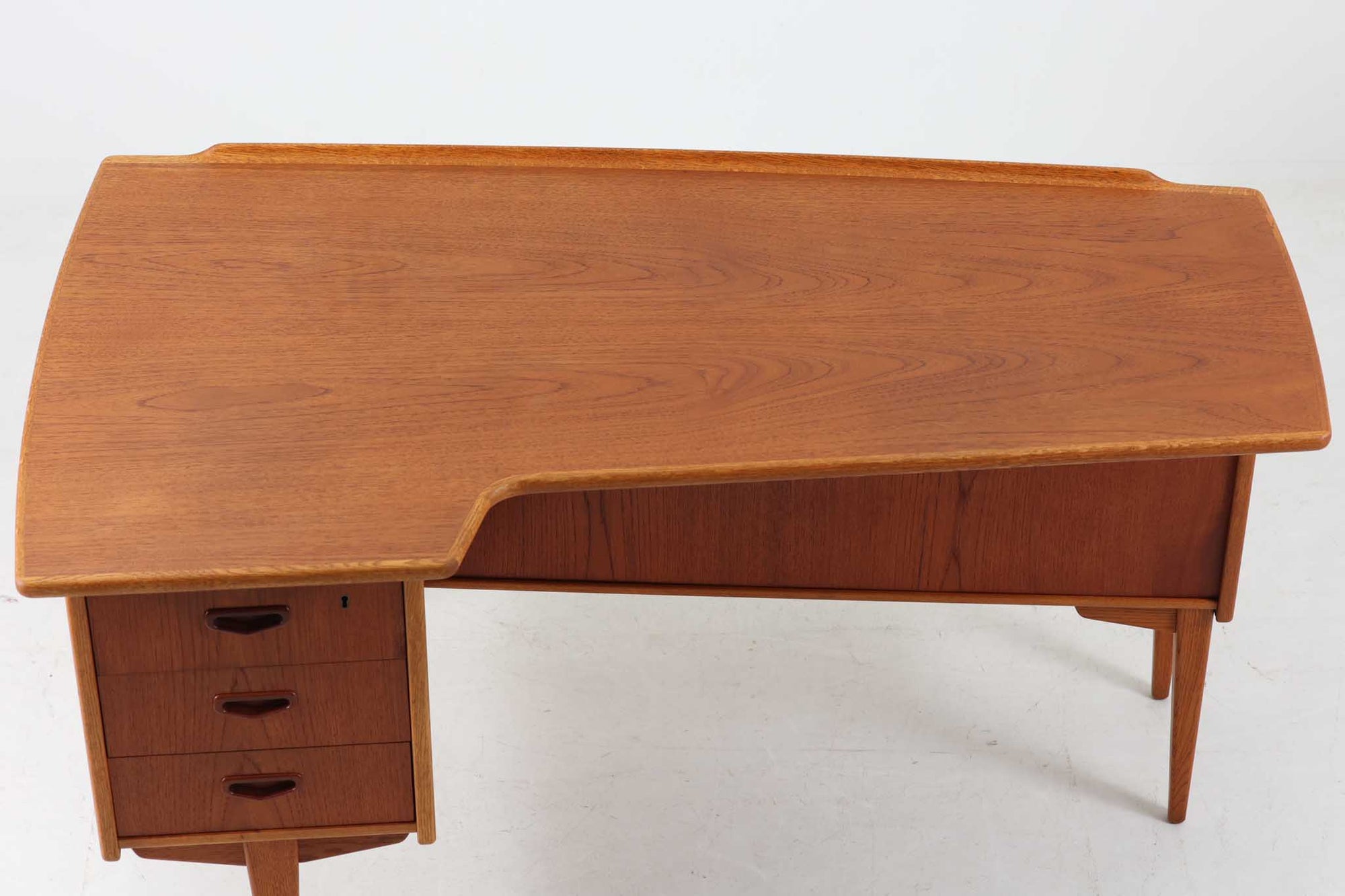 こちらはGoran Strandデザインのスウェーデン製ブーメラン型デスクで、Lelangs mobelfabrik社が製造したヴィンテージ家具です。チーク材とオーク材が使用されており、オーク材は脚や縁部分に施されており、スウェーデン家具らしい造りが特徴です。天板の奥側には返しがあり、実用性と美しさを兼ね備えています。デスクの後ろにはバックシェルフが設けられており、収納力も充実しています。温かみのある木材の組み合わせが、どんな空間にも調和し、優れた機能性とともに、ヴィンテージならではの魅力を感じさせてくれます。