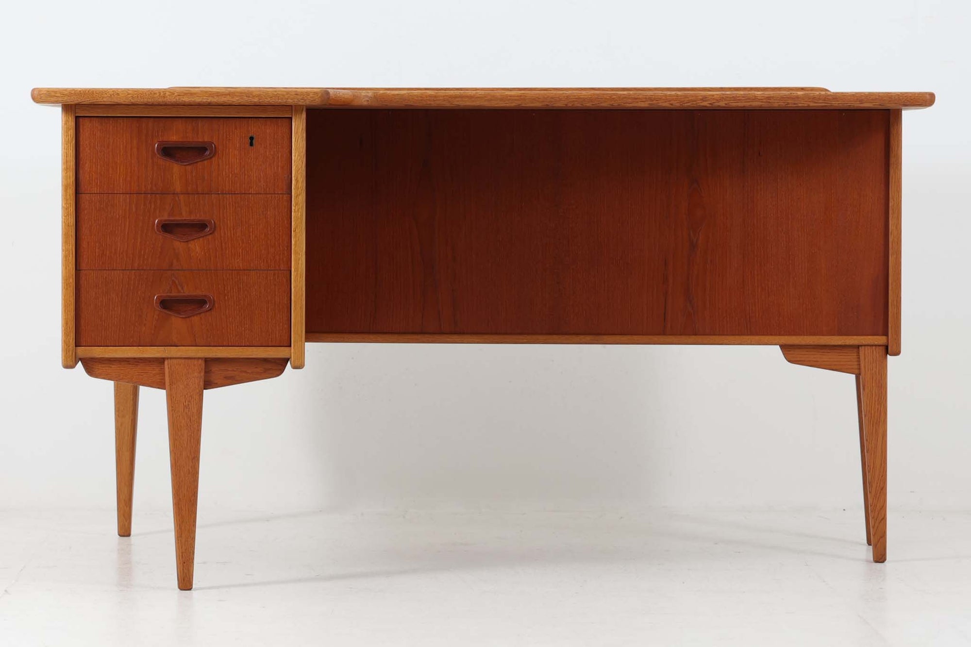 こちらはGoran Strandデザインのスウェーデン製ブーメラン型デスクで、Lelangs mobelfabrik社が製造したヴィンテージ家具です。チーク材とオーク材が使用されており、オーク材は脚や縁部分に施されており、スウェーデン家具らしい造りが特徴です。天板の奥側には返しがあり、実用性と美しさを兼ね備えています。デスクの後ろにはバックシェルフが設けられており、収納力も充実しています。温かみのある木材の組み合わせが、どんな空間にも調和し、優れた機能性とともに、ヴィンテージならではの魅力を感じさせてくれます。