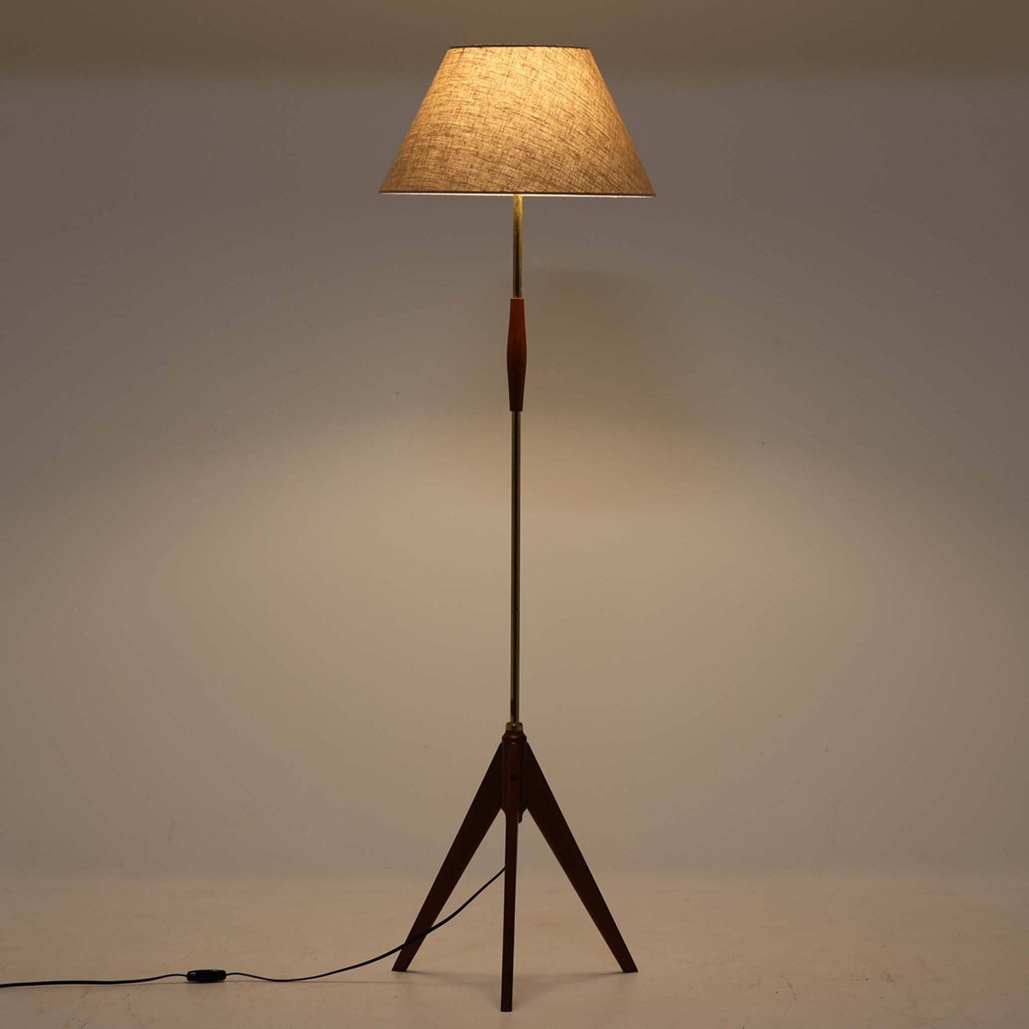 スウェーデンのOrsjo Armatur社による本作は、チーク材の三脚構造と真鍮色のスチール支柱が絶妙なバランスで組み合わされた、彫刻的な佇まいの北欧ビンテージフロアランプです。高さ136cmと扱いやすいサイズに加え、リネンシェードから柔らかく広がる光が空間に温かみを添えます。シンプルなフォルムの中に、素材の質感と構造美が宿る一台は、現代空間にも自然と溶け込む上質な照明です。