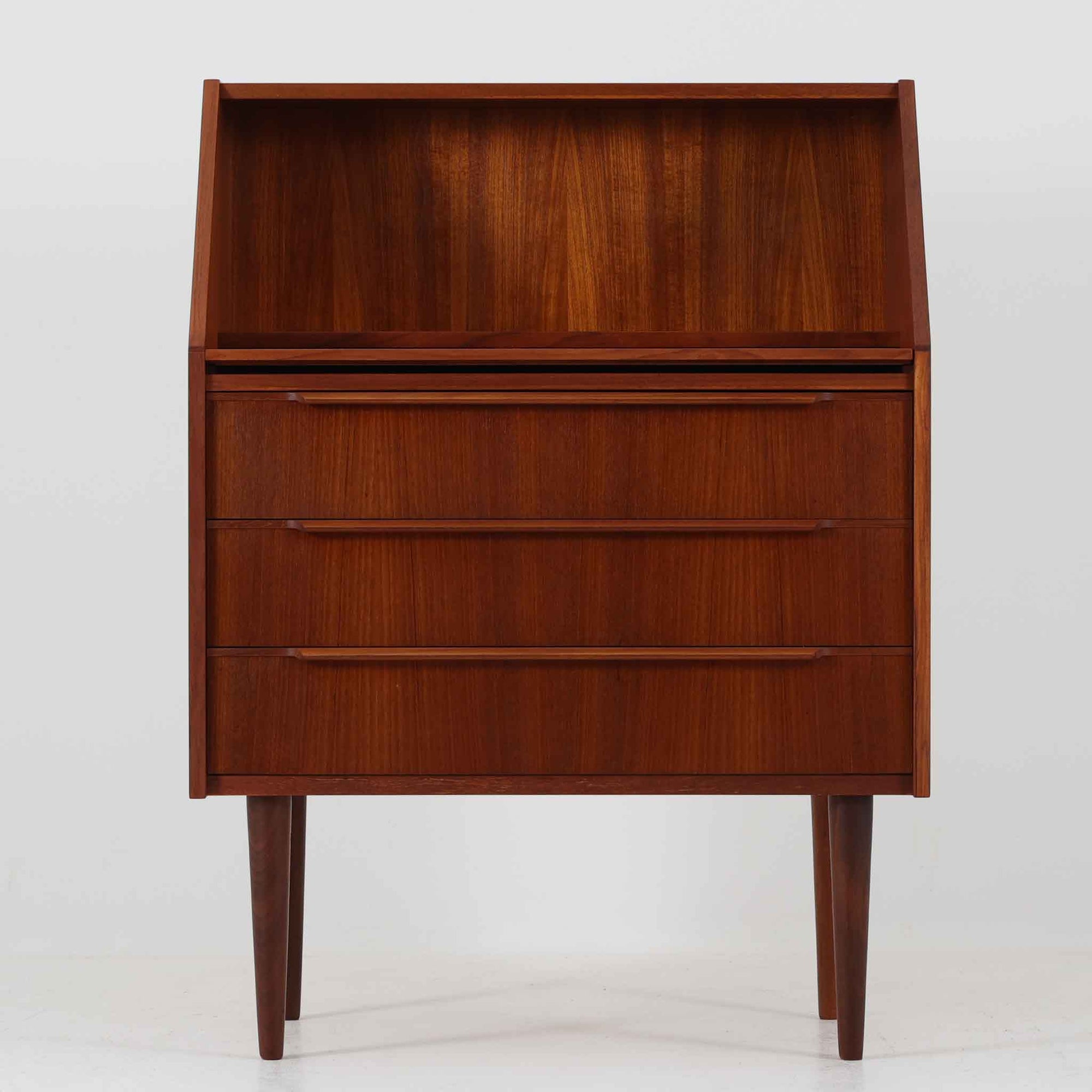 こちらのライティングビューロは、チーク材の美しい木目とシャープな脚部が印象的な北欧ビンテージ家具で、天板を手前に引き出すことでデスクスペースとしても使用できる実用的な構造です。上部には鏡が内蔵されており、使わない時はフラットに収納できる仕様で、ドレッサーとしても活躍します。3段の引き出しは十分な収納力を備え、細身の取手や無駄のないデザインが空間に洗練された雰囲気をもたらします。コンパクトながら多機能を備えた、希少な一台です。