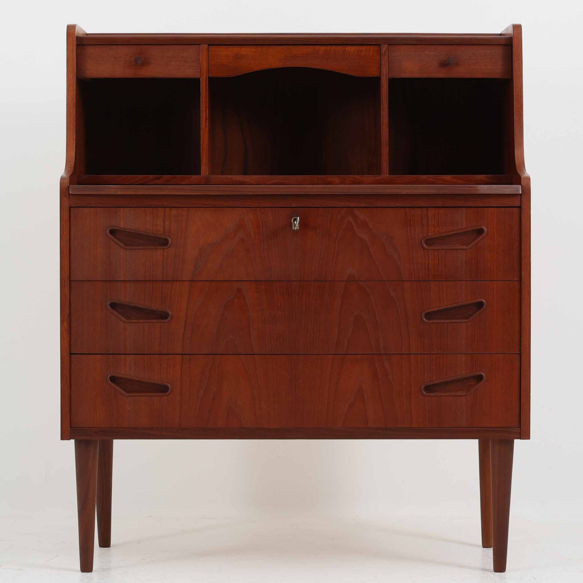 デンマーク製ライティングビューロです。上段には小引き出しと仕切り棚、中央には小さなミラーが備わり、書き物や身支度など多用途にお使いいただけます。チーク材の深みある色合いと滑らかな木目が美しく、シンプルで直線的なフォルムが落ち着いた印象を与えます。引き出しの斜めに削り出された取っ手やテーパー脚など、北欧らしい洗練されたディテールが魅力です。経年により増した艶が味わい深く、リビングや寝室に上品な温もりを添える一台です。