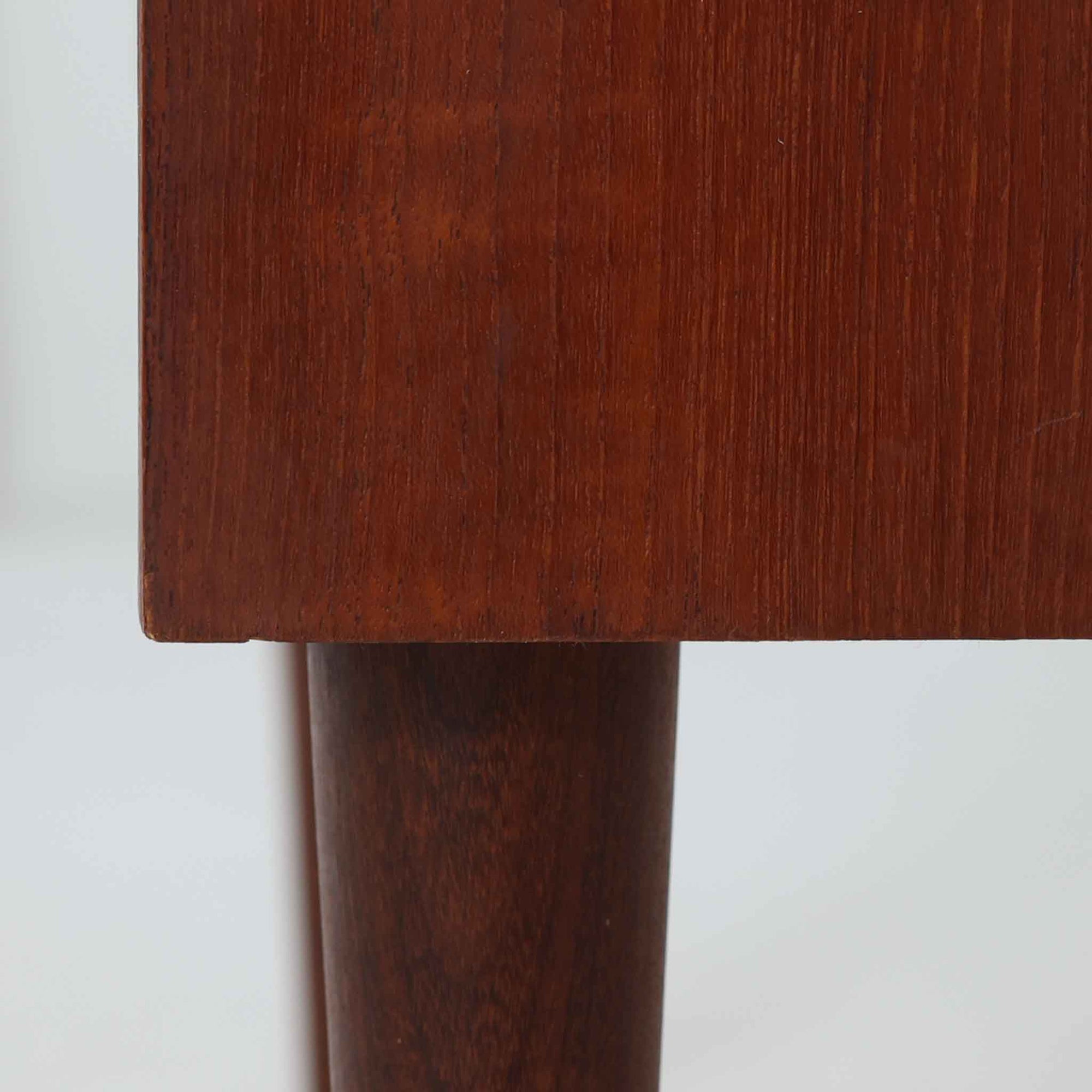 デンマーク製ライティングビューロです。上段には小引き出しと仕切り棚、中央には小さなミラーが備わり、書き物や身支度など多用途にお使いいただけます。チーク材の深みある色合いと滑らかな木目が美しく、シンプルで直線的なフォルムが落ち着いた印象を与えます。引き出しの斜めに削り出された取っ手やテーパー脚など、北欧らしい洗練されたディテールが魅力です。経年により増した艶が味わい深く、リビングや寝室に上品な温もりを添える一台です。