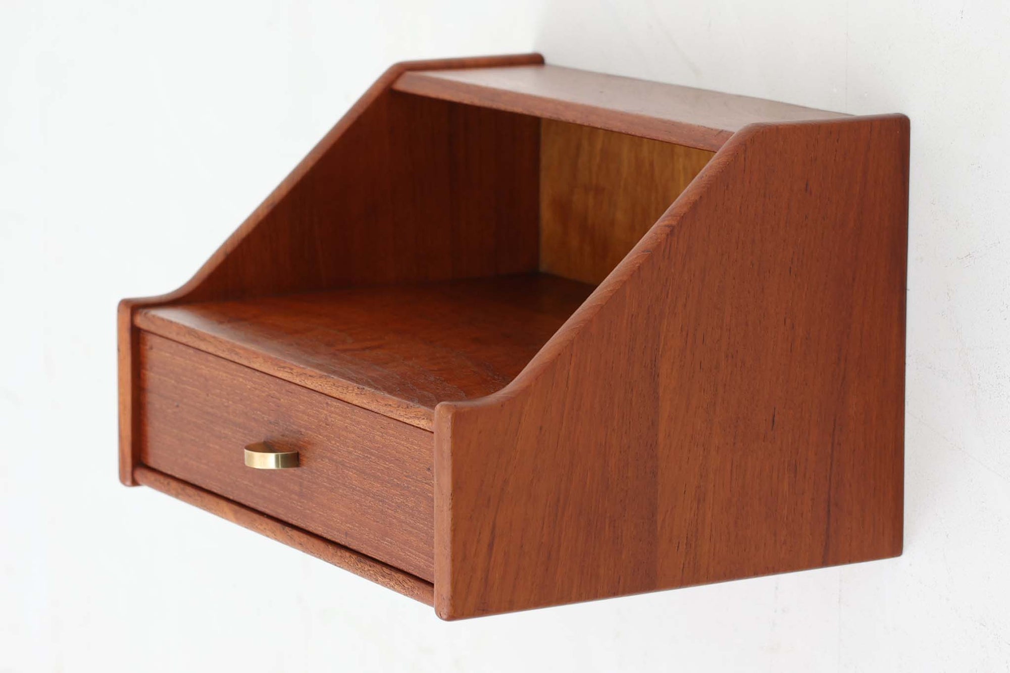北欧より買い付けたウォールシェルフ。良質なチーク材が贅沢に使用され、経年変化によって深みを増した色味が魅力です。引き出しの小さなゴールド色の取手がデザインのアクセントとなっています。引き出し1段、天板と引き出しの間には物を置けるスペースもあり、リビングや寝室、オフィスの壁面収納にぴったり。飾り棚としても、小物の整理にも活躍します。
