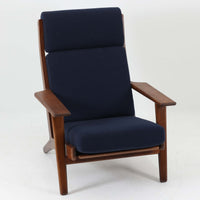 Hans J. Wegnerがデザインし、Getamaが製作したGE290Aハイバックシングルソファです。ダークオーク材の堅牢なフレームは丸みを帯びたアームと後方へ傾斜した脚部が特徴で、身体をやさしく受け止める構造美が際立ちます。張り替えられた落ち着いた色調のクッションは、内部にビンテージ特有のスプリングを内包し、程よい弾力と快適な座り心地を実現。読書や寛ぎの時間に最適で、経年により深みを増した木部の質感が北欧ビンテージならではの存在感と上質な雰囲気を空間に添える一脚です。