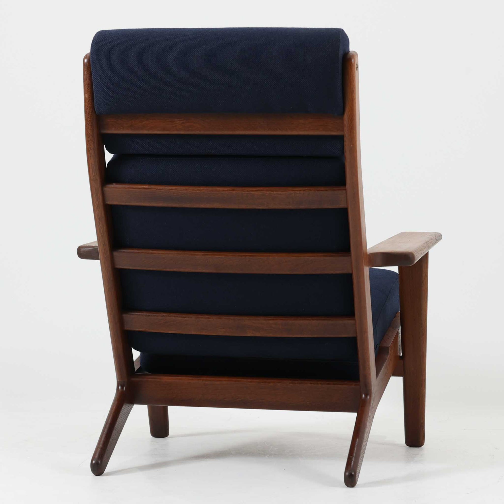 Hans J. Wegnerがデザインし、Getamaが製作したGE290Aハイバックシングルソファです。ダークオーク材の堅牢なフレームは丸みを帯びたアームと後方へ傾斜した脚部が特徴で、身体をやさしく受け止める構造美が際立ちます。張り替えられた落ち着いた色調のクッションは、内部にビンテージ特有のスプリングを内包し、程よい弾力と快適な座り心地を実現。読書や寛ぎの時間に最適で、経年により深みを増した木部の質感が北欧ビンテージならではの存在感と上質な雰囲気を空間に添える一脚です。