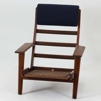 Hans J. Wegnerがデザインし、Getamaが製作したGE290Aハイバックシングルソファです。ダークオーク材の堅牢なフレームは丸みを帯びたアームと後方へ傾斜した脚部が特徴で、身体をやさしく受け止める構造美が際立ちます。張り替えられた落ち着いた色調のクッションは、内部にビンテージ特有のスプリングを内包し、程よい弾力と快適な座り心地を実現。読書や寛ぎの時間に最適で、経年により深みを増した木部の質感が北欧ビンテージならではの存在感と上質な雰囲気を空間に添える一脚です。