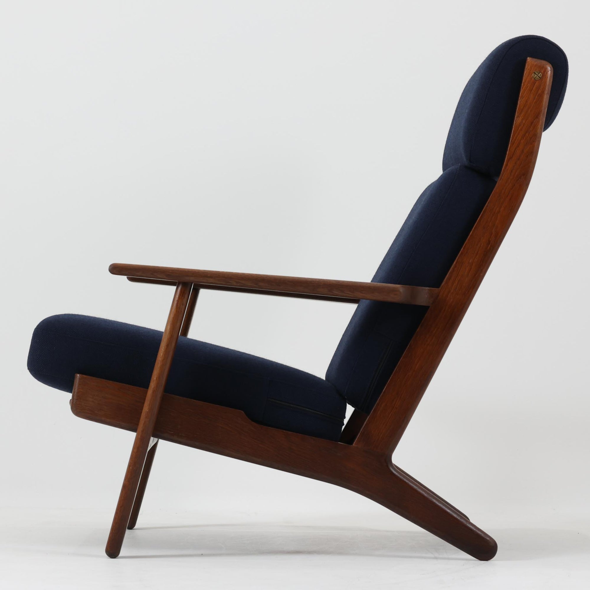 Hans J. Wegnerがデザインし、Getamaが製作したGE290Aハイバックシングルソファです。ダークオーク材の堅牢なフレームは丸みを帯びたアームと後方へ傾斜した脚部が特徴で、身体をやさしく受け止める構造美が際立ちます。張り替えられた落ち着いた色調のクッションは、内部にビンテージ特有のスプリングを内包し、程よい弾力と快適な座り心地を実現。読書や寛ぎの時間に最適で、経年により深みを増した木部の質感が北欧ビンテージならではの存在感と上質な雰囲気を空間に添える一脚です。