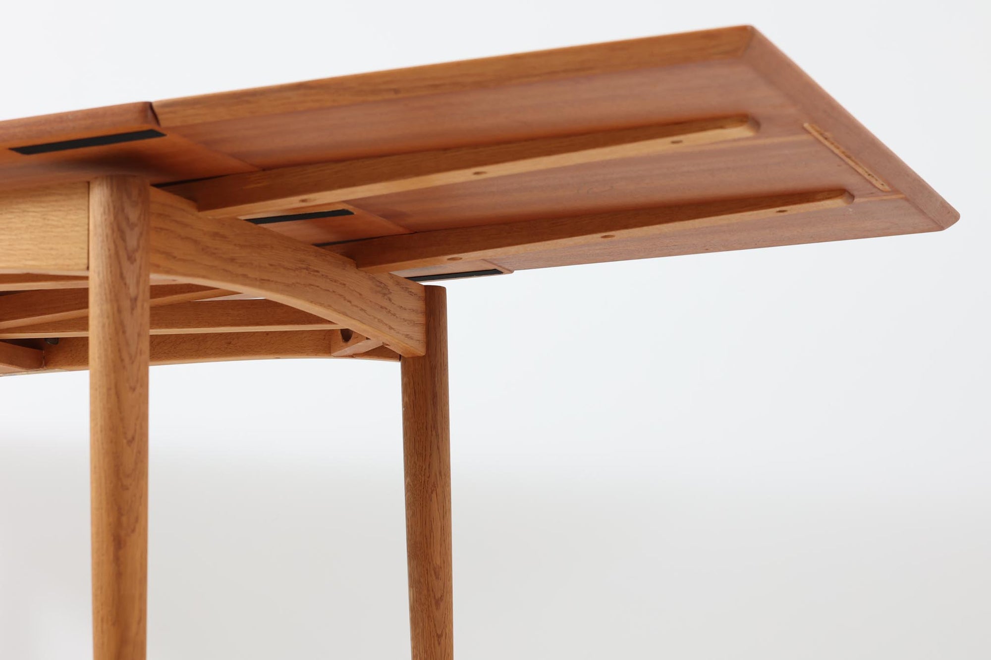 デンマークの名工Slagelse mobelvaerk社が手掛けたこちらのダイニングテーブルは、アーチ状の幕板が特徴であり、異なる素材の組み合わせが美しさを際立たせます。天板には上質なチーク材が用いられ、脚部にはナチュラルなオーク材が採用されています。また、幕板は強度と使い勝手が考慮され、通常時には4人、拡張時には6～8人が快適に使用できる設計となっています。