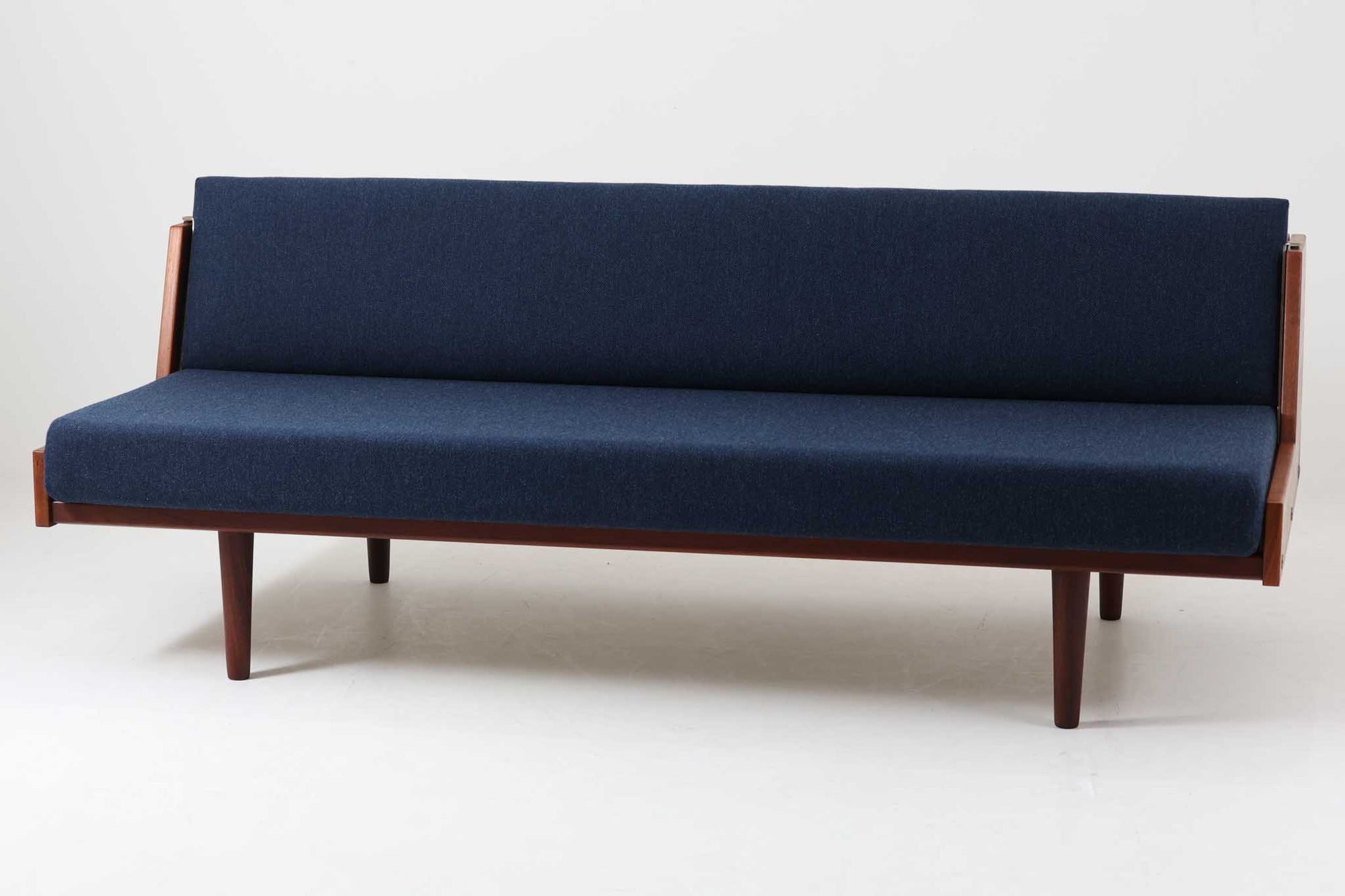 デンマークの名門家具メーカーGetama（ゲタマ）より、Hans J. Wegner（ハンス・J・ウェグナー）によってデザインされたビンテージのデイベッド「GE258」のご紹介です。チーク材のフレームに、希少な丸脚仕様が特徴的なモデルで、無駄のない美しい直線と有機的なフォルムが融合した北欧モダンデザインの代表作です。背もたれを後方に倒すことでベッドとしてもご使用いただける実用性の高い構造で、張地は落ち着いたネイビー系のファブリックで張り替え済みです。チーク材の木目が美しく、経年による味わいも感じられる逸品です。