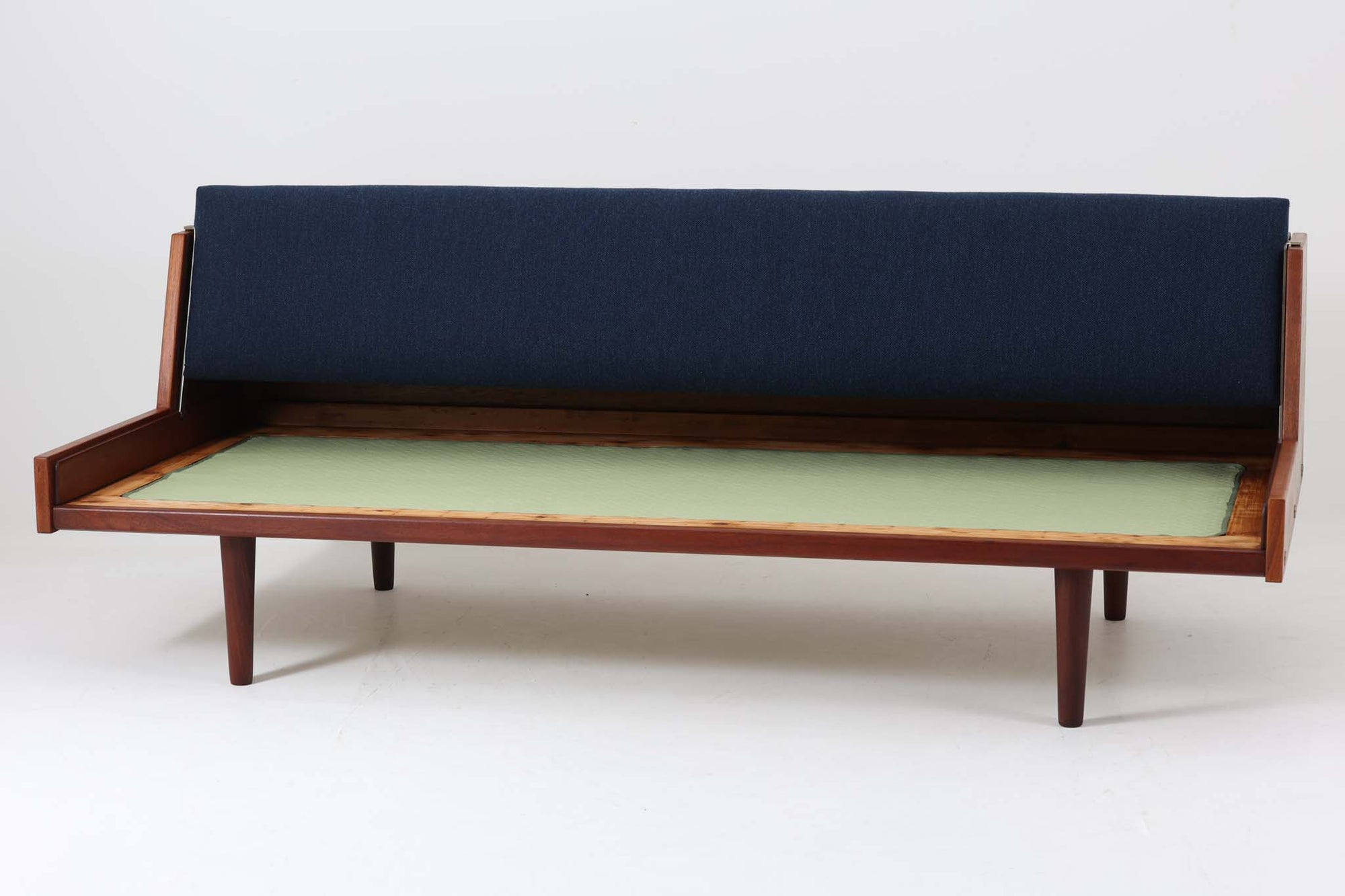 デンマークの名門家具メーカーGetama（ゲタマ）より、Hans J. Wegner（ハンス・J・ウェグナー）によってデザインされたビンテージのデイベッド「GE258」のご紹介です。チーク材のフレームに、希少な丸脚仕様が特徴的なモデルで、無駄のない美しい直線と有機的なフォルムが融合した北欧モダンデザインの代表作です。背もたれを後方に倒すことでベッドとしてもご使用いただける実用性の高い構造で、張地は落ち着いたネイビー系のファブリックで張り替え済みです。チーク材の木目が美しく、経年による味わいも感じられる逸品です。