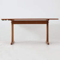 Borge Mogensen（ボーエ・モーエンセン）がFDB Moblerのために手掛けたC18ダイニングテーブルは、チーク材天板とオーク材脚部を組み合わせた北欧モダンを象徴するビンテージ家具で、直線的で端正なプロポーションと安定感のあるT字脚構造が特徴です。拡張板を備え、来客時や家族構成の変化にも柔軟に対応でき、日常使いから特別な食卓まで幅広く活躍します。現在はCarl Hansen & Son社より復刻生産されていますが、チーク材天板とオーク材脚部という素材の組み合わせは当時のビンテージ品ならではの仕様で、脚部に用いられた真鍮製の留め具も現行品とは異なる形状となっています。経年により深みを増した木肌と、実用性を重視したモーエンセンらしい設計思想、そしてビンテージならではのディテールを味わえる一台です。