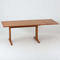 Borge Mogensen（ボーエ・モーエンセン）がFDB Moblerのために手掛けたC18ダイニングテーブルは、チーク材天板とオーク材脚部を組み合わせた北欧モダンを象徴するビンテージ家具で、直線的で端正なプロポーションと安定感のあるT字脚構造が特徴です。拡張板を備え、来客時や家族構成の変化にも柔軟に対応でき、日常使いから特別な食卓まで幅広く活躍します。現在はCarl Hansen & Son社より復刻生産されていますが、チーク材天板とオーク材脚部という素材の組み合わせは当時のビンテージ品ならではの仕様で、脚部に用いられた真鍮製の留め具も現行品とは異なる形状となっています。経年により深みを増した木肌と、実用性を重視したモーエンセンらしい設計思想、そしてビンテージならではのディテールを味わえる一台です。