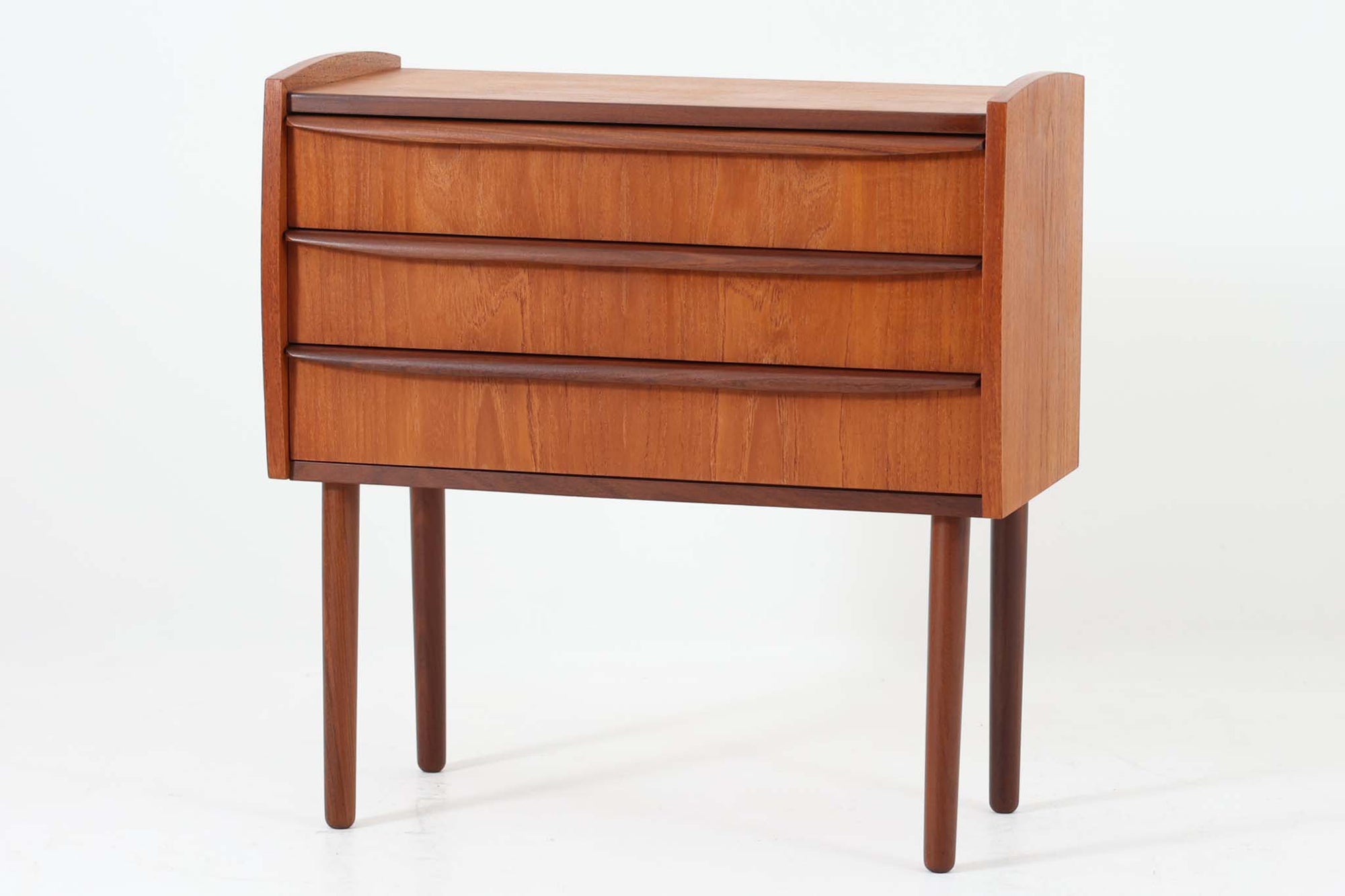 特徴的な丸みを帯びた側板と、典型的なデンマーク家具らしいバータイプの取手が素敵なデザインです。また、天板の両側面は物が落ちにくいように出っ張っており、実用性も考慮されています。本体には上質なチーク材が使用されています。使い勝手の良い小ぶりなサイズ感です。