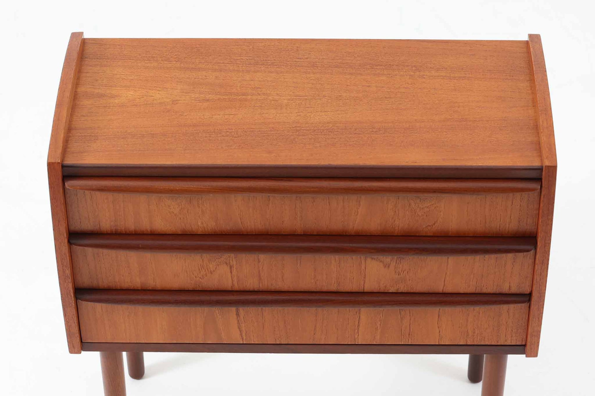 特徴的な丸みを帯びた側板と、典型的なデンマーク家具らしいバータイプの取手が素敵なデザインです。また、天板の両側面は物が落ちにくいように出っ張っており、実用性も考慮されています。本体には上質なチーク材が使用されています。使い勝手の良い小ぶりなサイズ感です。