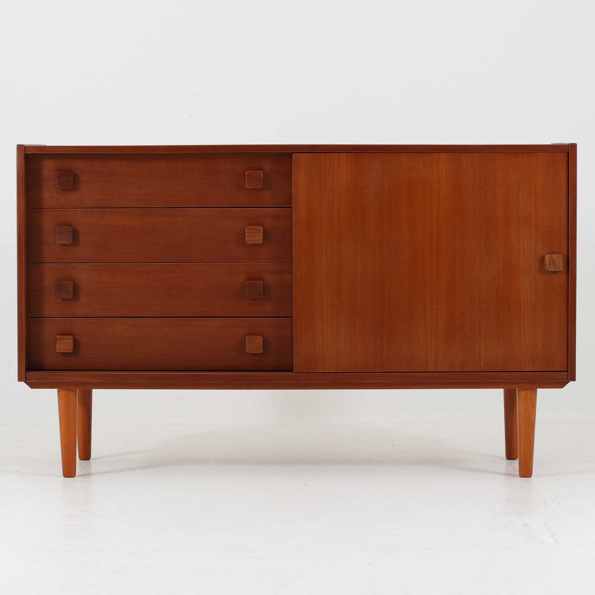 Domino Mobler社製のサイドボードは、北欧デンマークのビンテージ家具らしいシンプルかつ機能的なデザインが魅力です。チーク材を用いた温かみのある木目と深みのある色調が空間に落ち着きを与えます。左側には4杯の引き出し、右側にはスライド扉付きの収納棚を備え、食器や日用品をすっきり収めることが可能です。特徴的なスクエア型の木製ハンドルや細身の脚部が洗練された印象を与え、ダイニングやリビングでの収納家具としてだけでなく、テレビボードや飾り棚としても活躍する実用性と存在感を兼ね備えています。年月を経た風合いがより一層の魅力を引き立てる逸品です。