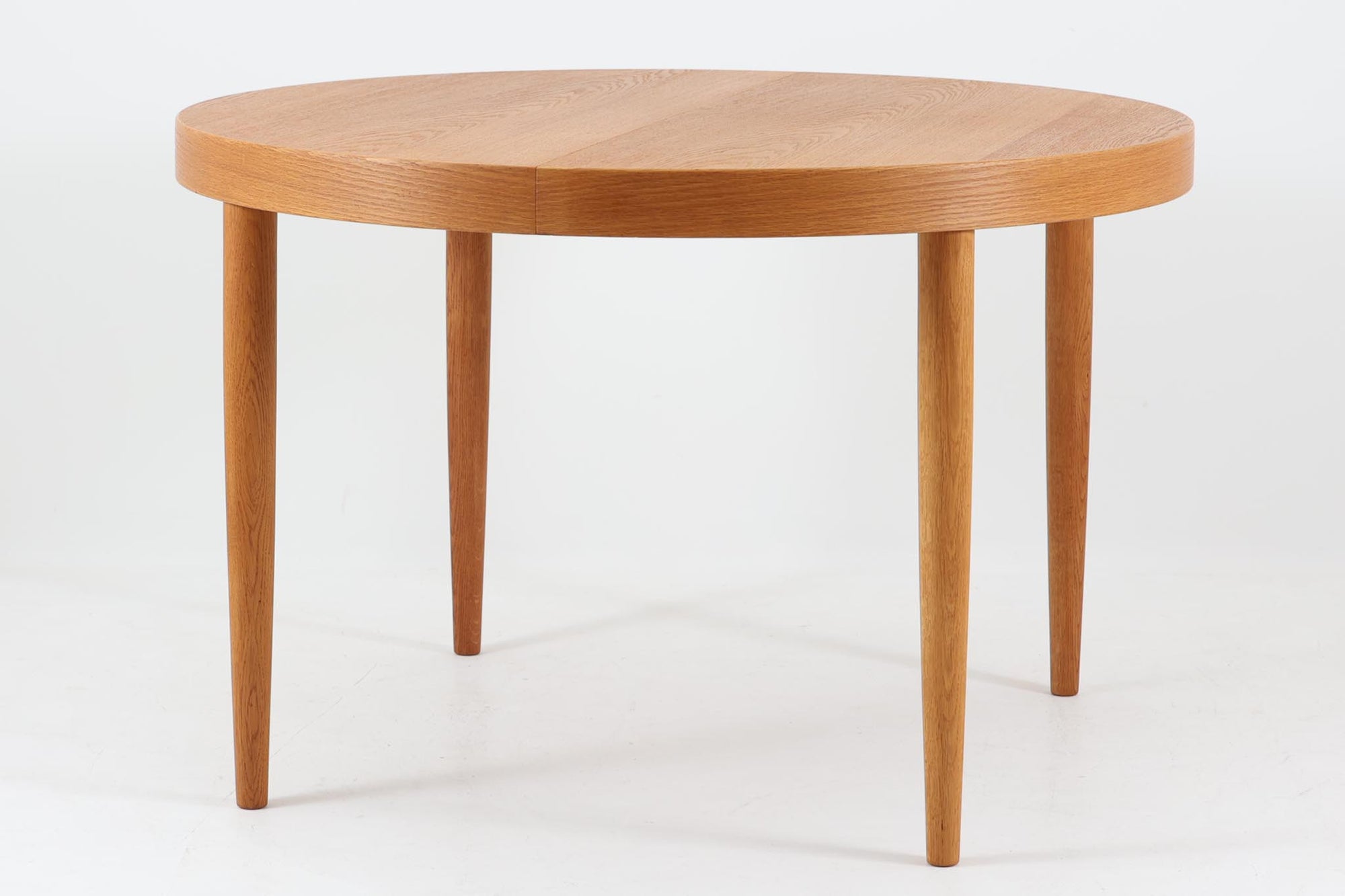 美しい木目のオーク材で作られたデンマーク製のビンテージダイニングテーブルです。シンプルでありながら北欧らしい洗練されたデザインが魅力で、エクステンション機能により天板を伸長して大人数にも対応可能です。天板を閉じた状態では直径のある円形テーブルとして、拡張時には楕円形になり広々とご使用いただけます。丸みを帯びた天板のエッジと先細りの脚が軽やかで、どんな空間にも調和します。Danish Controlの刻印も確認でき、品質の高さが伺える逸品です。北欧モダンな空間演出におすすめの一台です。